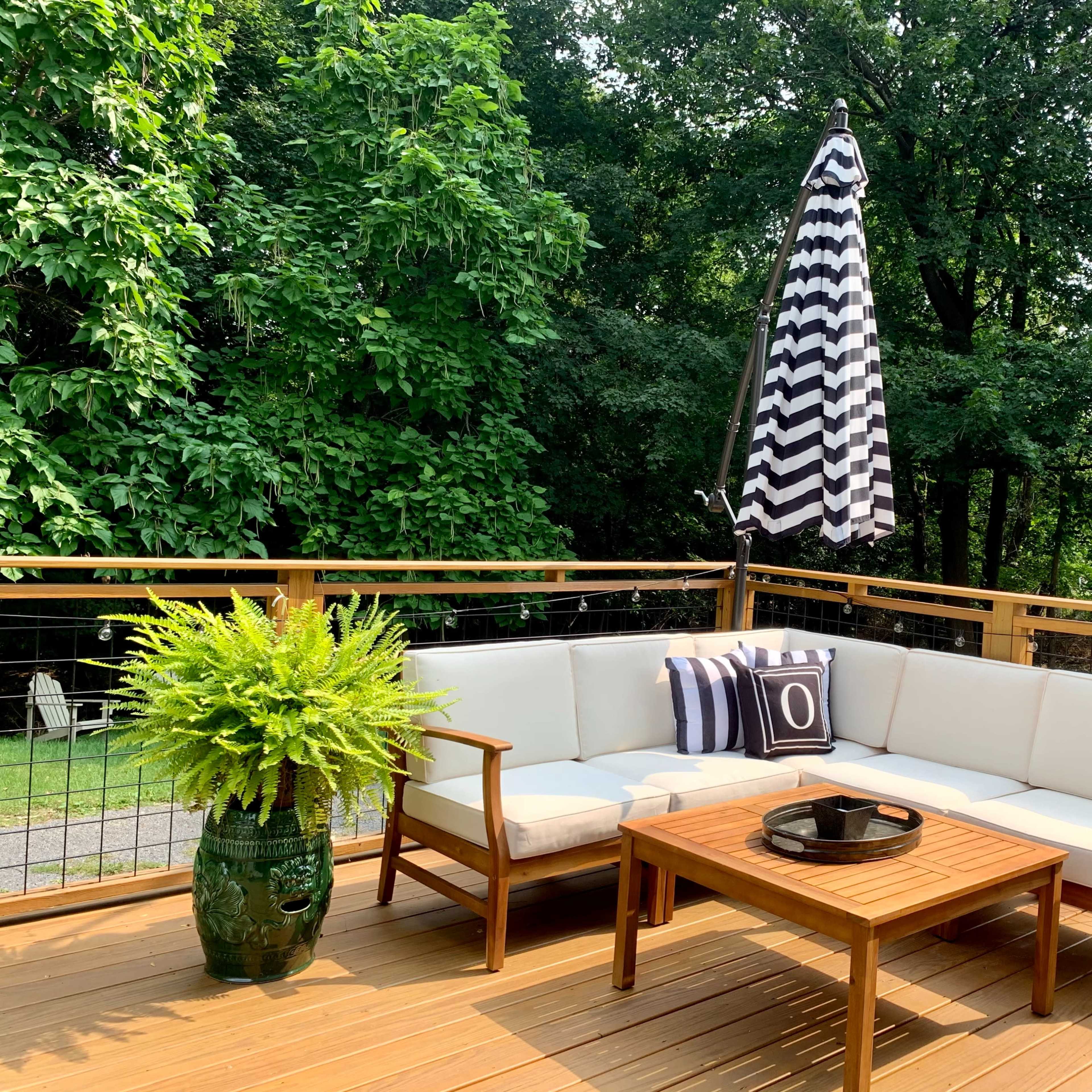 A patio seating area features a sectional sofa with a coffee table, surrounded by greenery and a large striped umbrella.