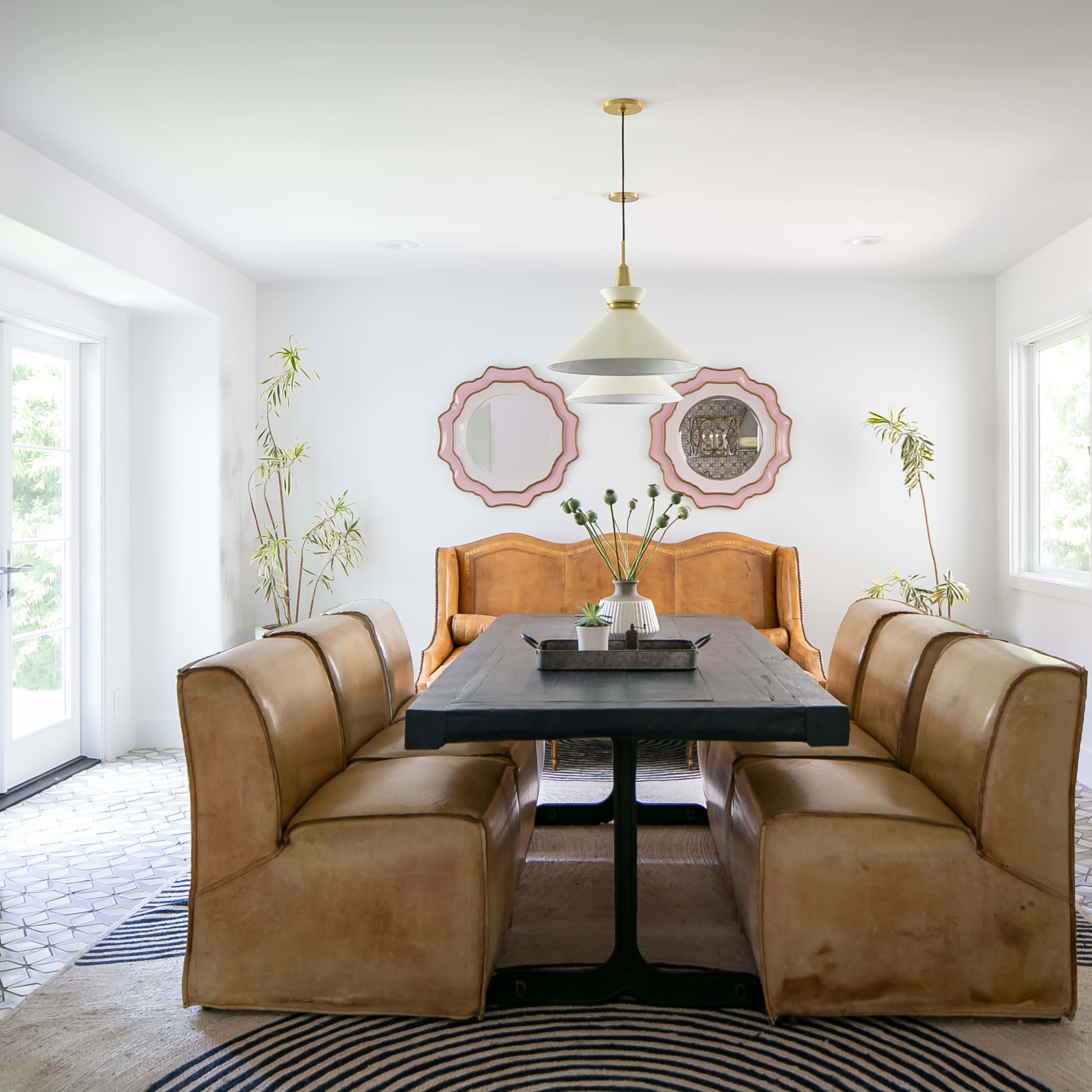 A dining room features a large black table surrounded by leather chairs, with a light fixture above and decorative mirrors on the walls.