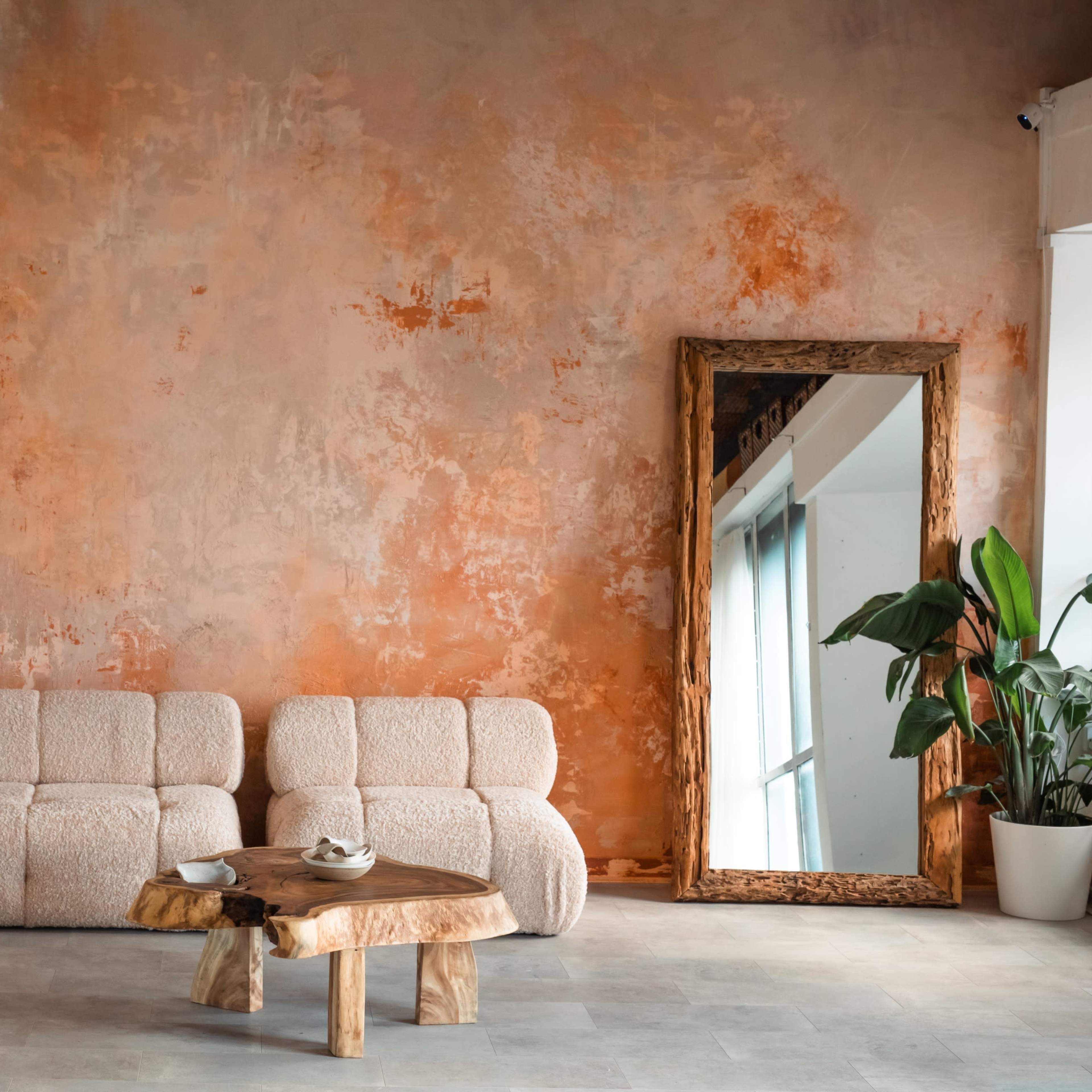 A cozy living space features a textured orange wall, two plush sofas, a wooden coffee table, and decorative plants in white pots.