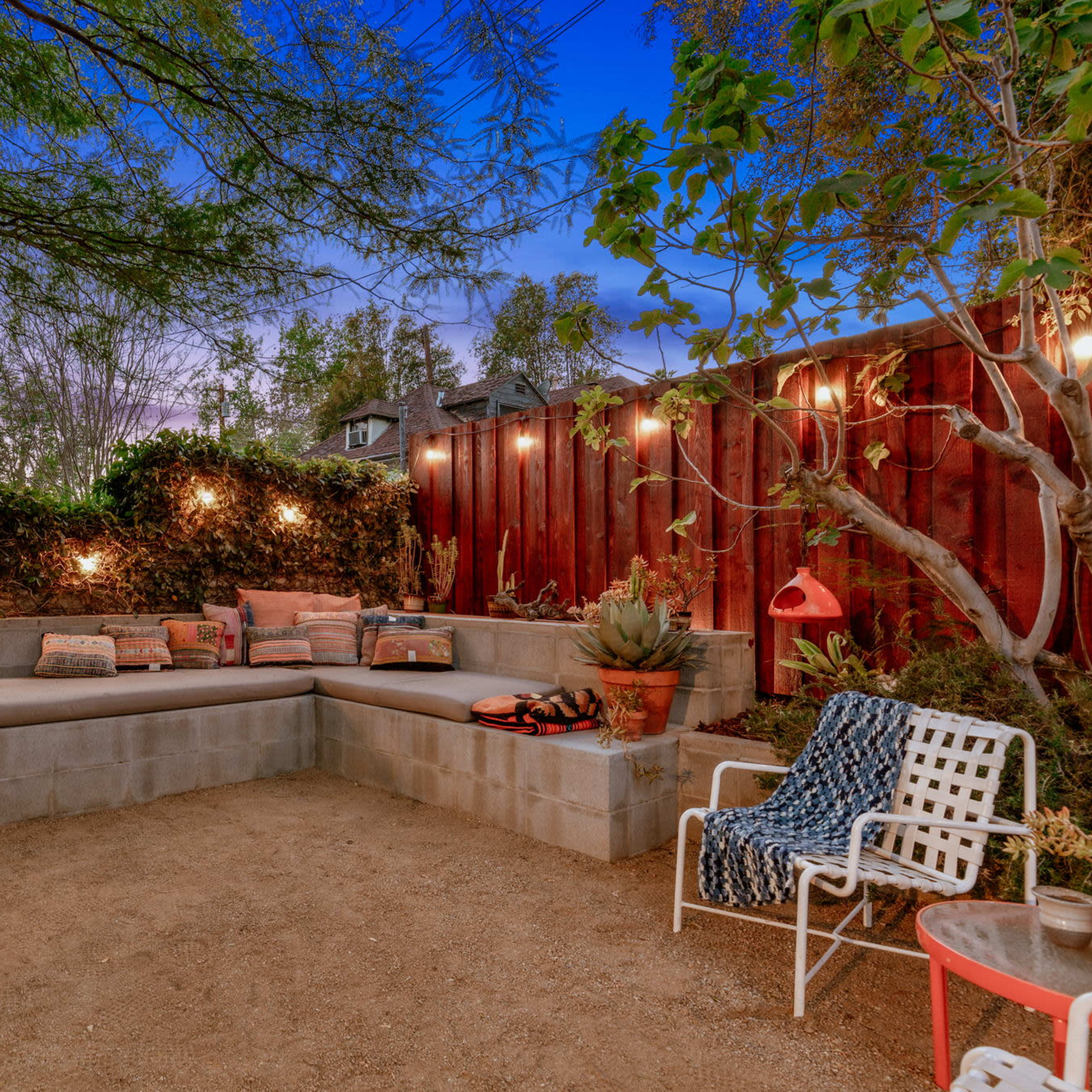 A cozy outdoor seating area with a concrete wall bench, string lights, and various plants in a gravel landscape.