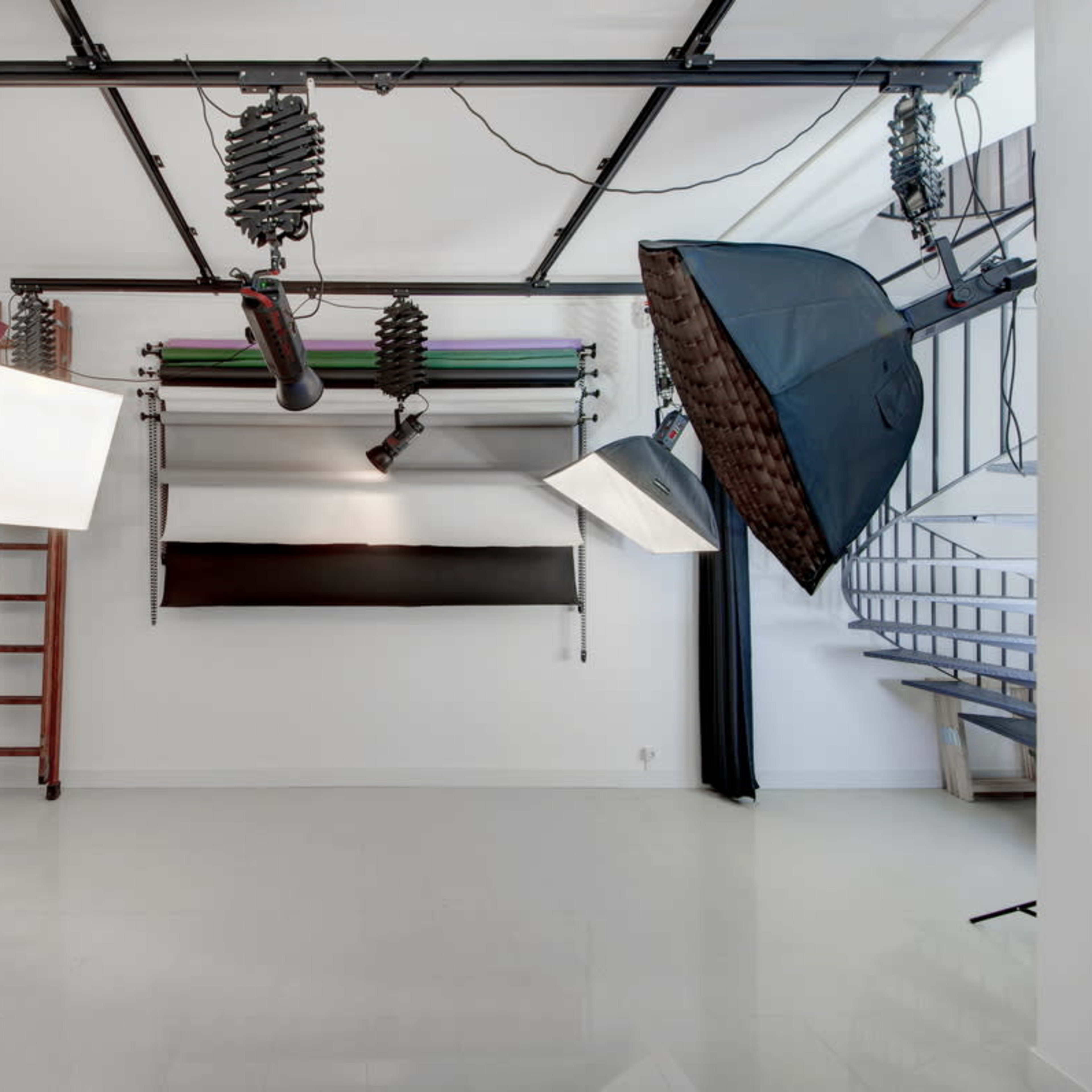 A well-lit photography studio equipped with various lighting setups, including softboxes and a ladder, against a minimalist background.