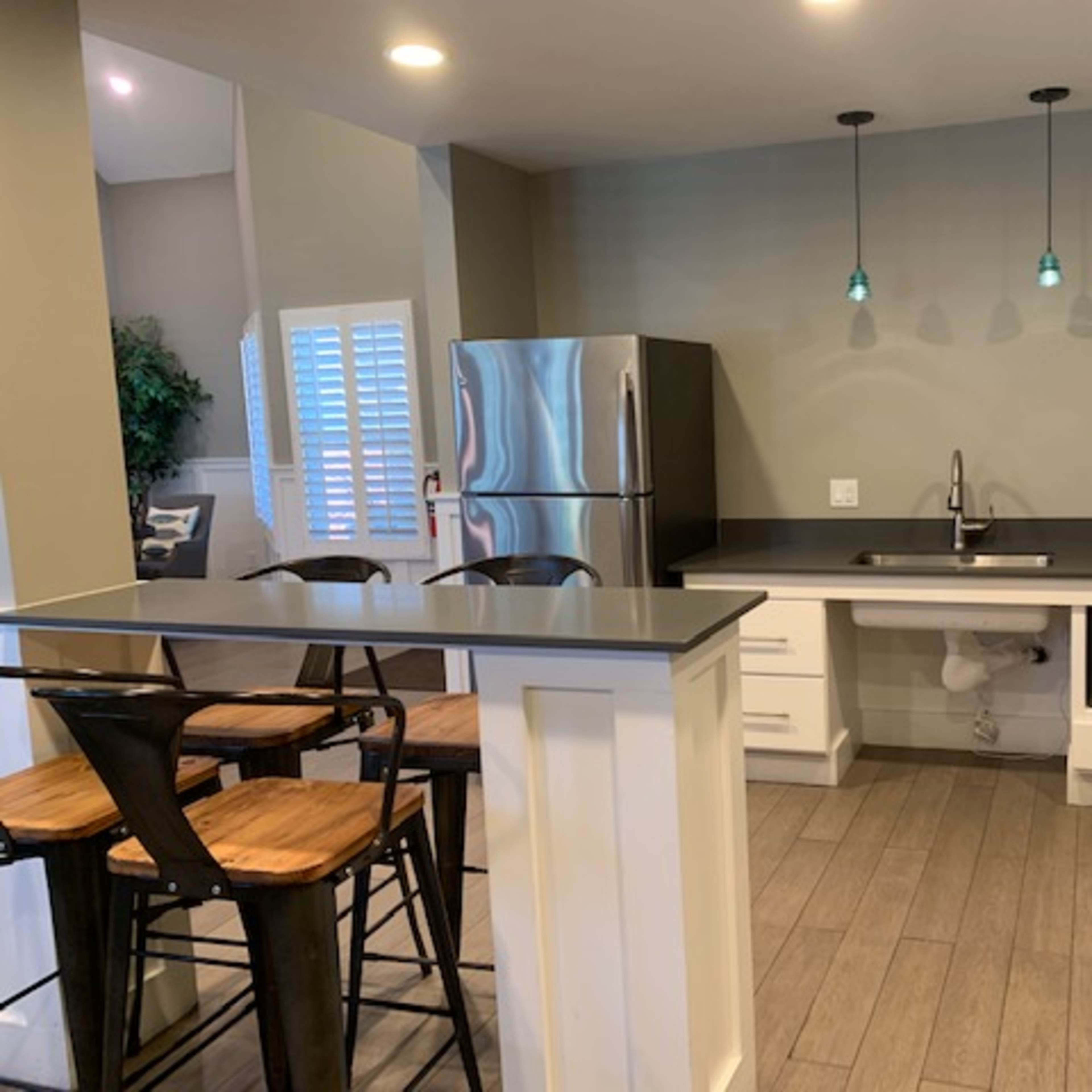 A modern kitchen with stainless steel appliances, a gray countertop, bar seating, and pendant lights above the sink.