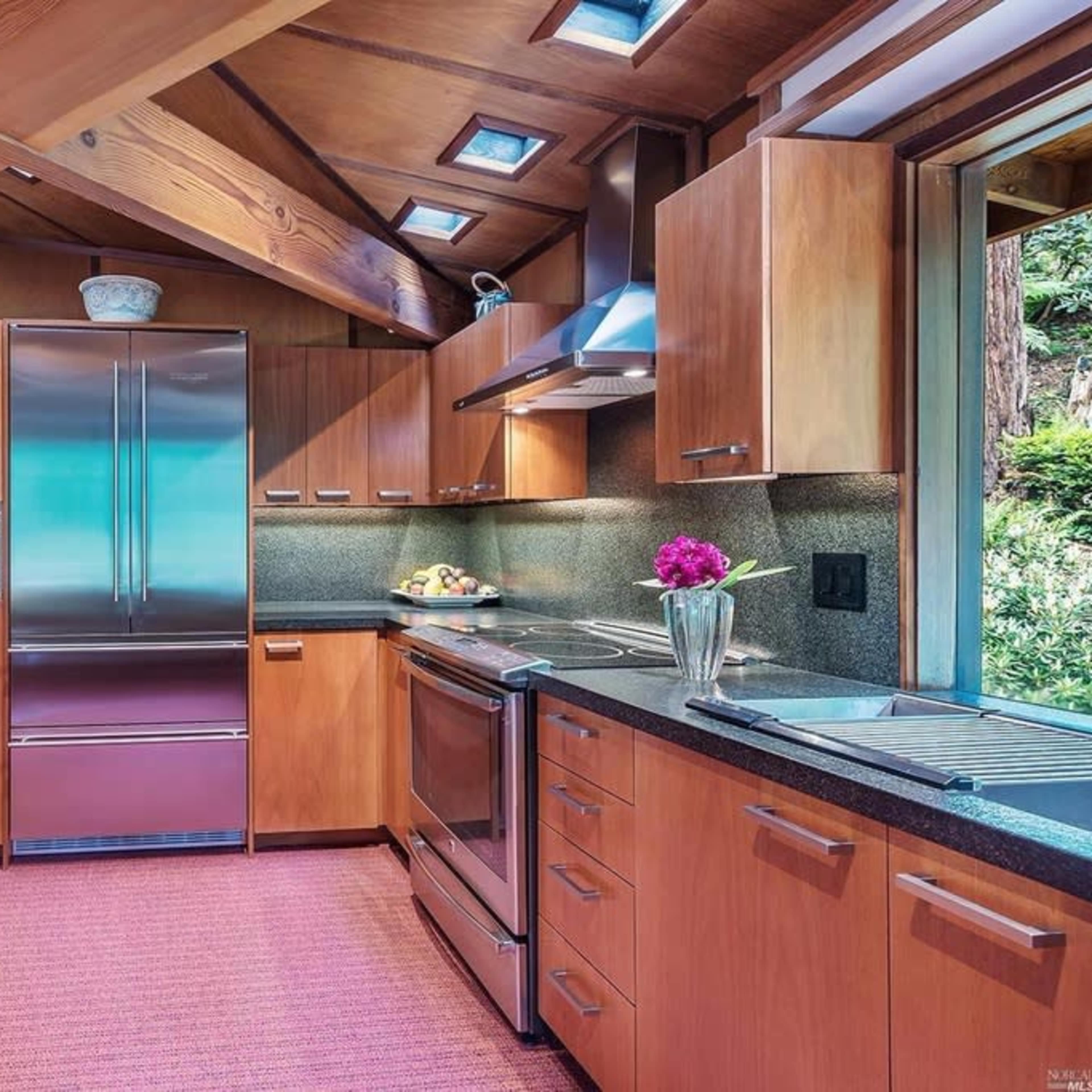 A modern kitchen features wooden cabinets, stainless steel appliances, and a countertop with a small flower arrangement.