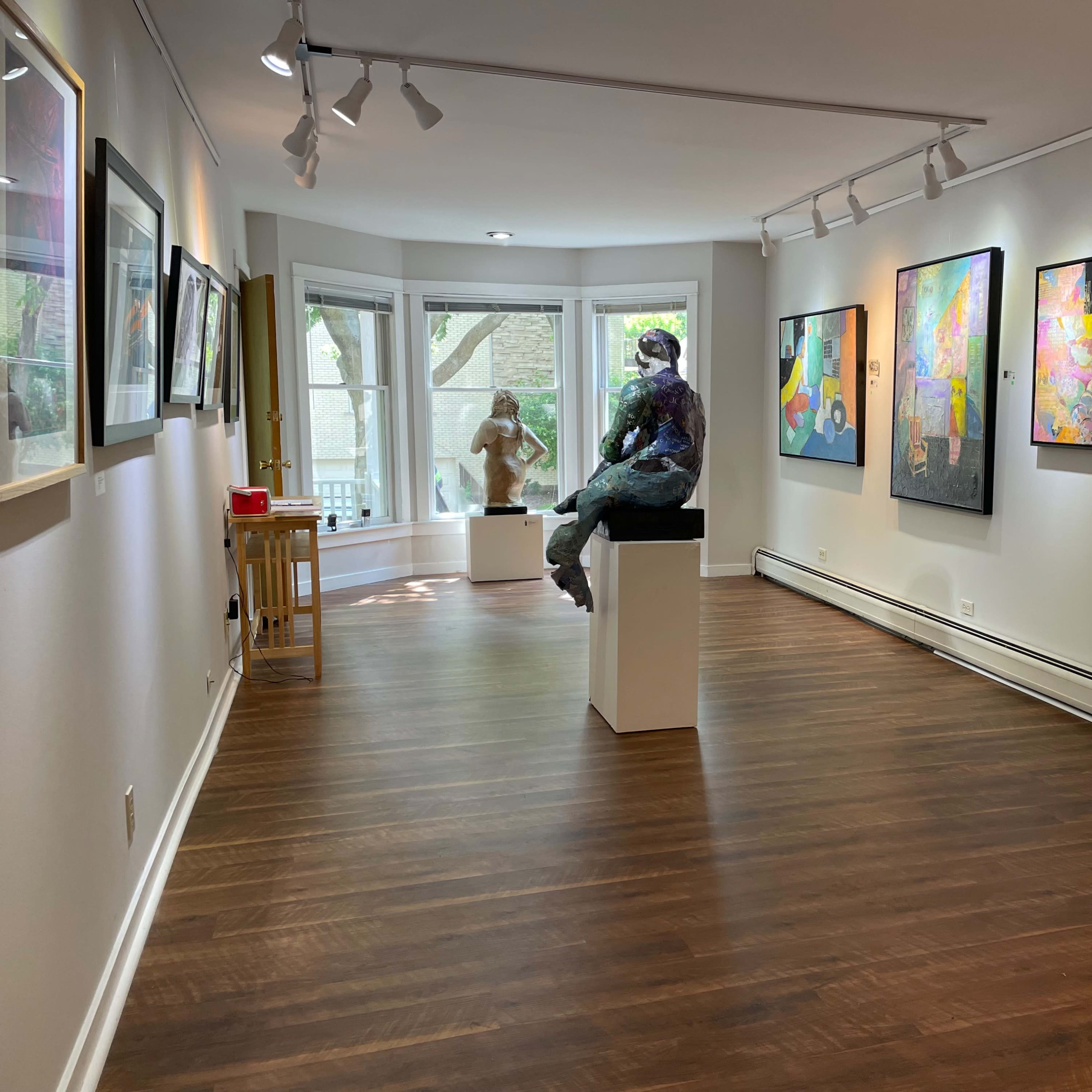 An art gallery featuring a sculpture on a pedestal and various colorful paintings hanging on the white walls.