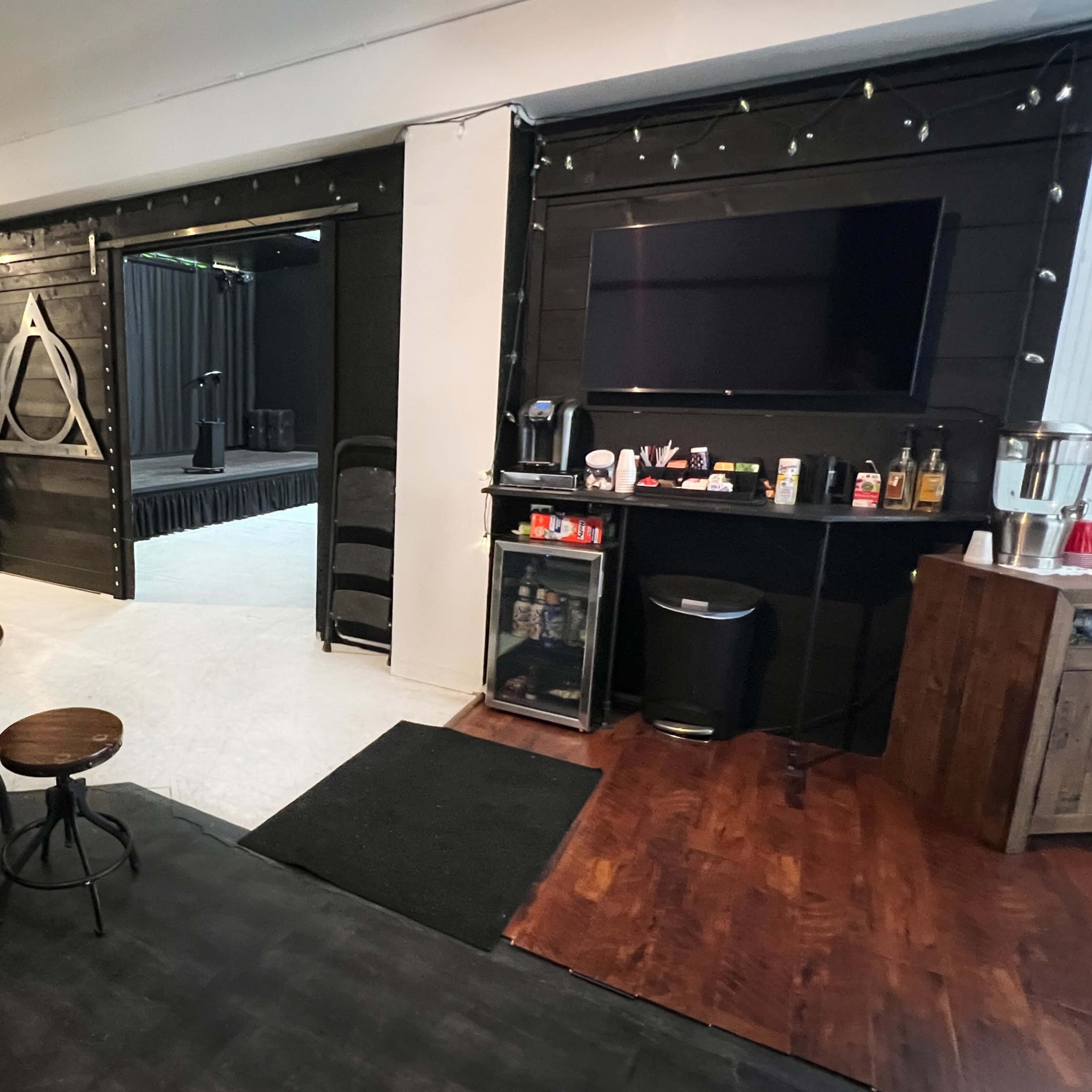 A modern, open space featuring a seating area with wooden furniture, a coffee station, and a stage set up in the background.