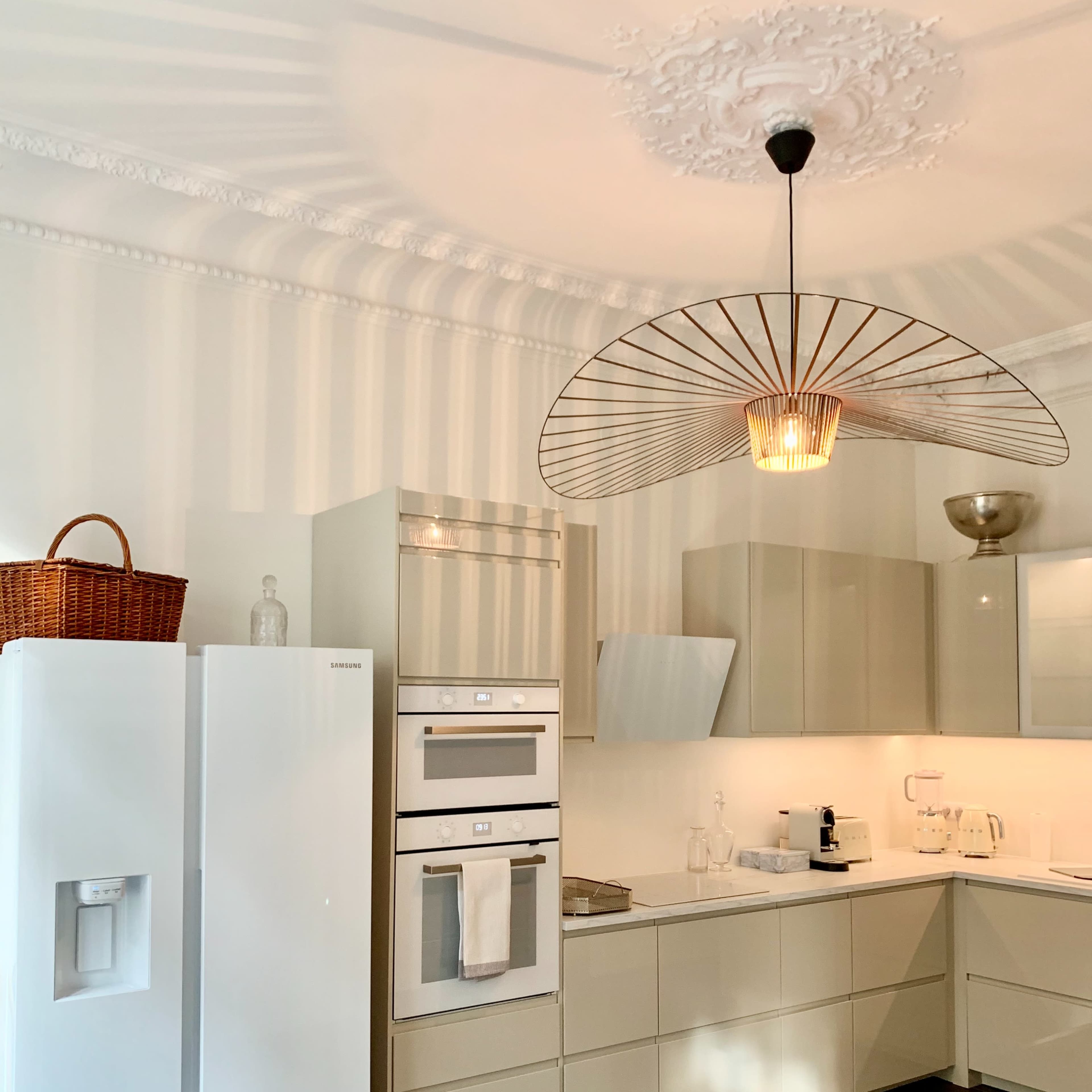 A modern kitchen with light-colored cabinets, a white refrigerator, and a large pendant light.
