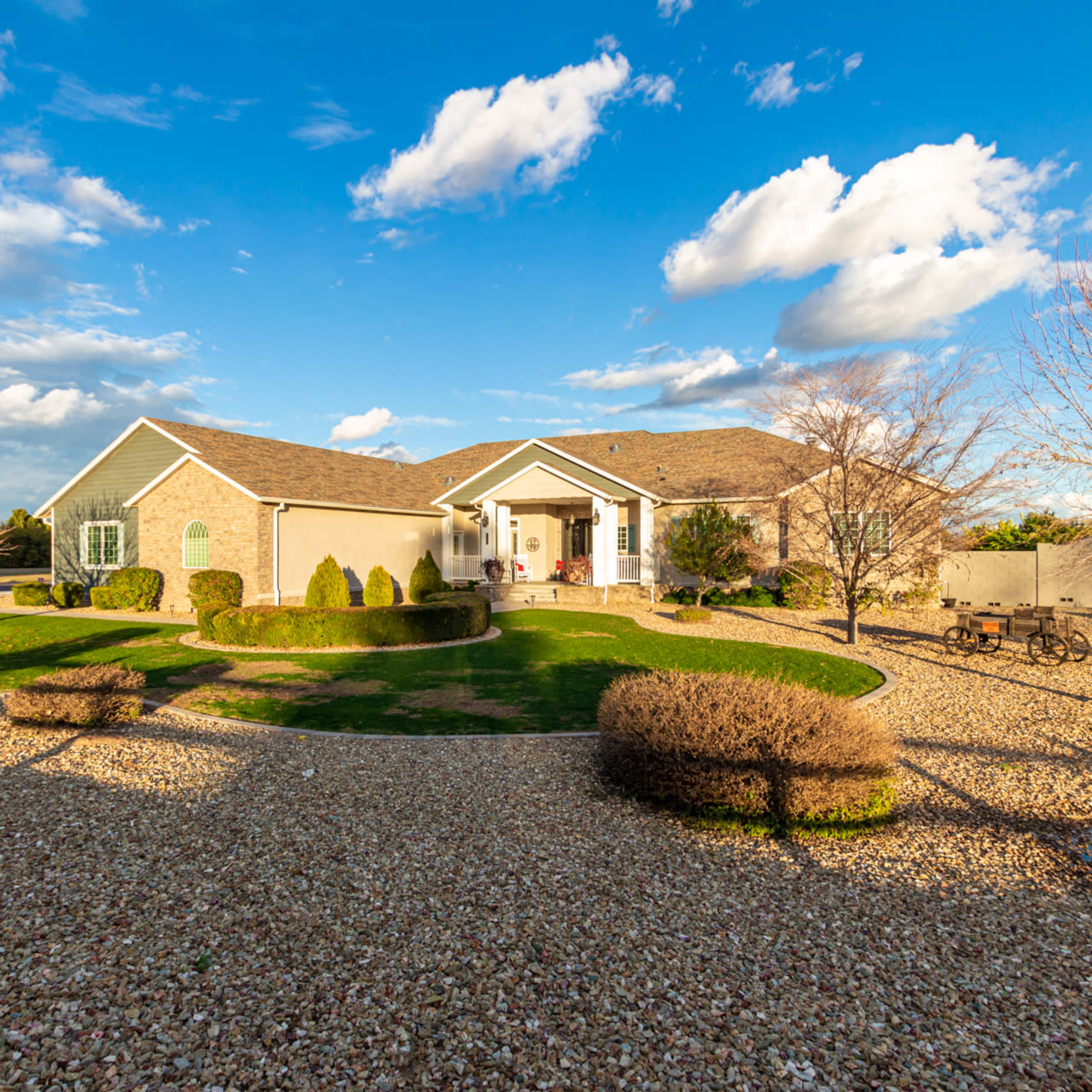 A well-landscaped home features a large front yard with gravel pathways, trimmed bushes, and a porch under partly cloudy skies.