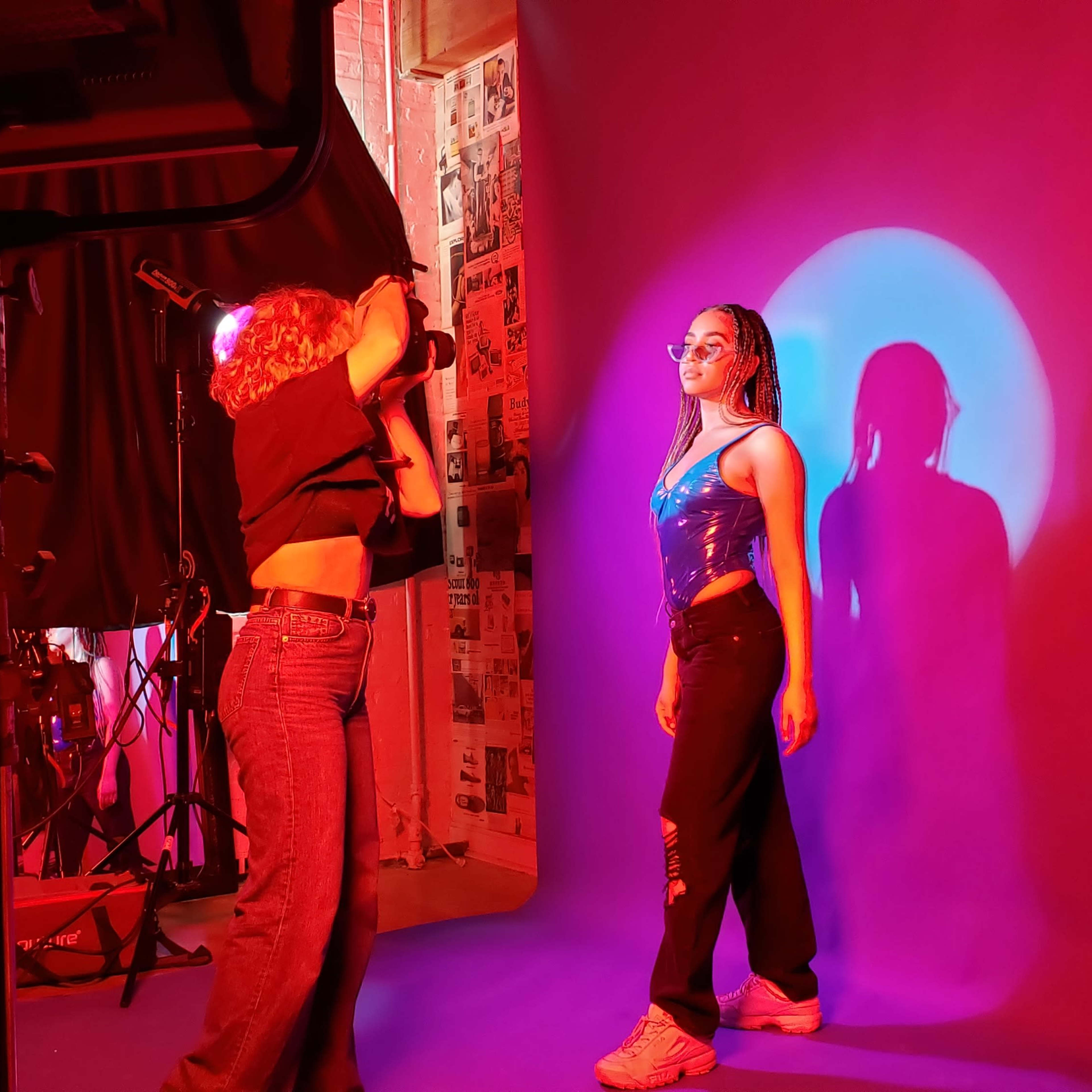 A photographer captures a model posing against a brightly lit purple backdrop in a studio setting.