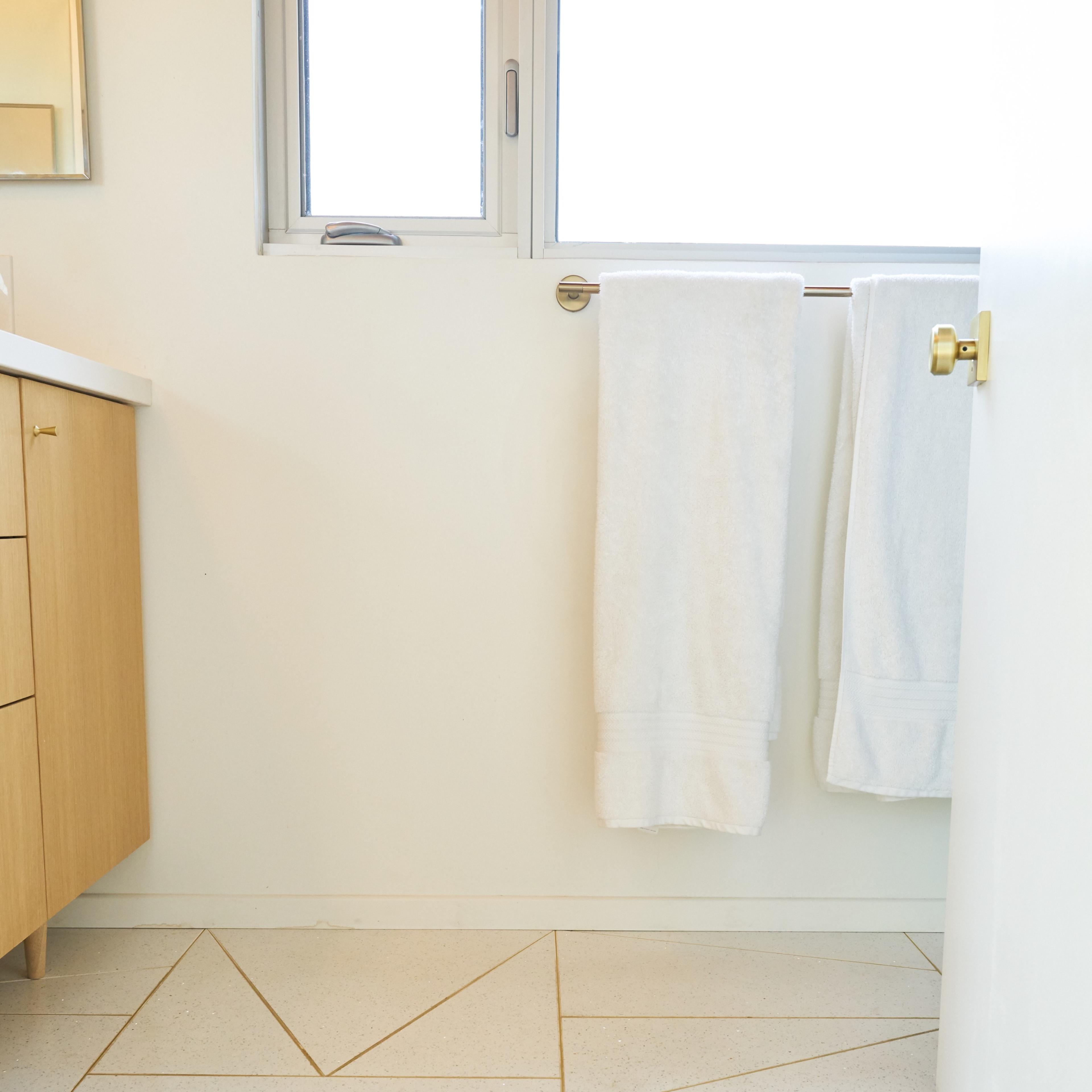A bathroom floor featuring geometric tile patterns, with two white towels hanging near a window and a wooden vanity cabinet.