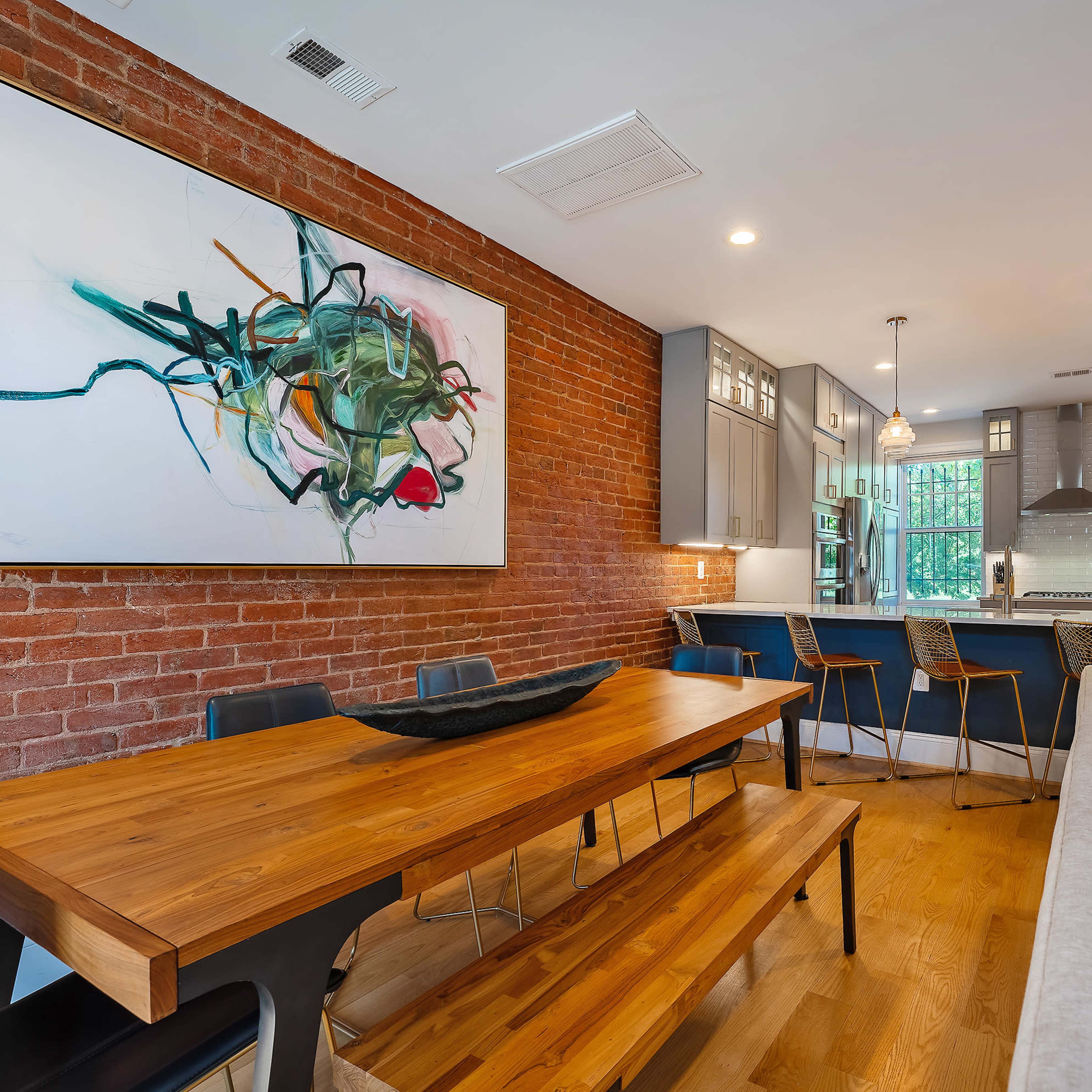 A modern living and dining area with a wooden dining table, brick walls, and a kitchen visible in the background.