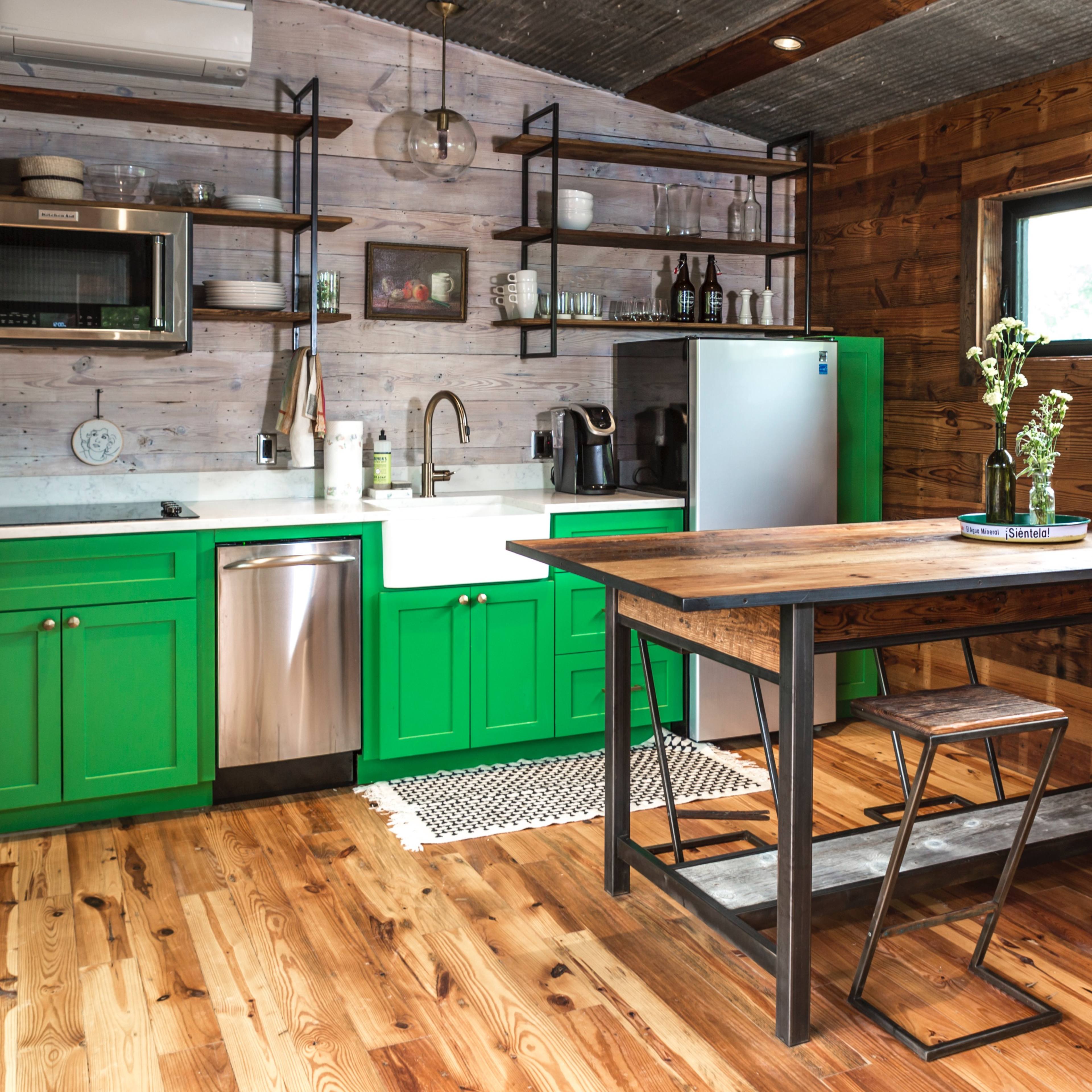 A modern kitchen featuring bright green cabinetry, stainless steel appliances, wooden countertops, and a wooden dining table with metal stools.