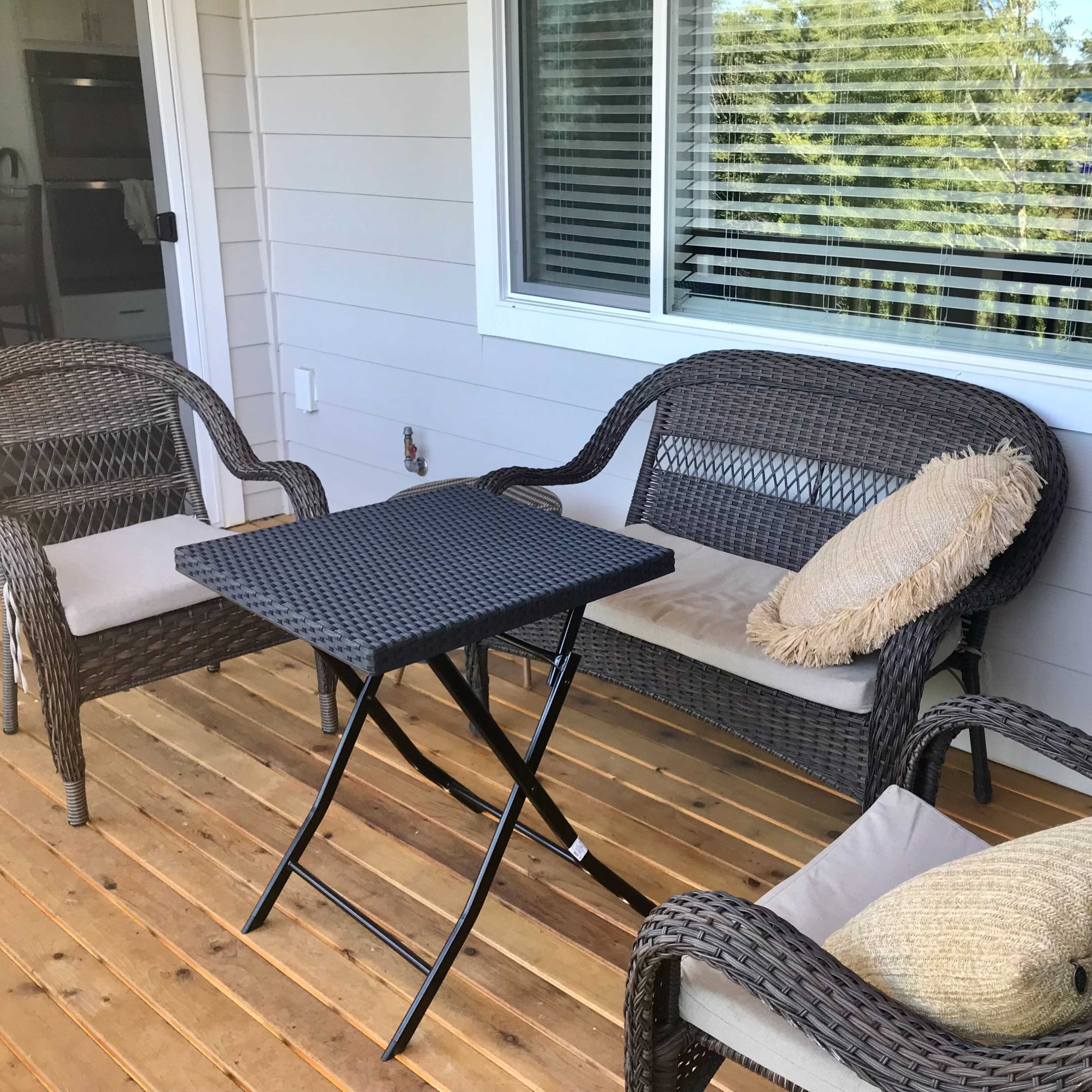 A small outdoor seating area features two chairs and a table made of dark wicker on a wooden deck.