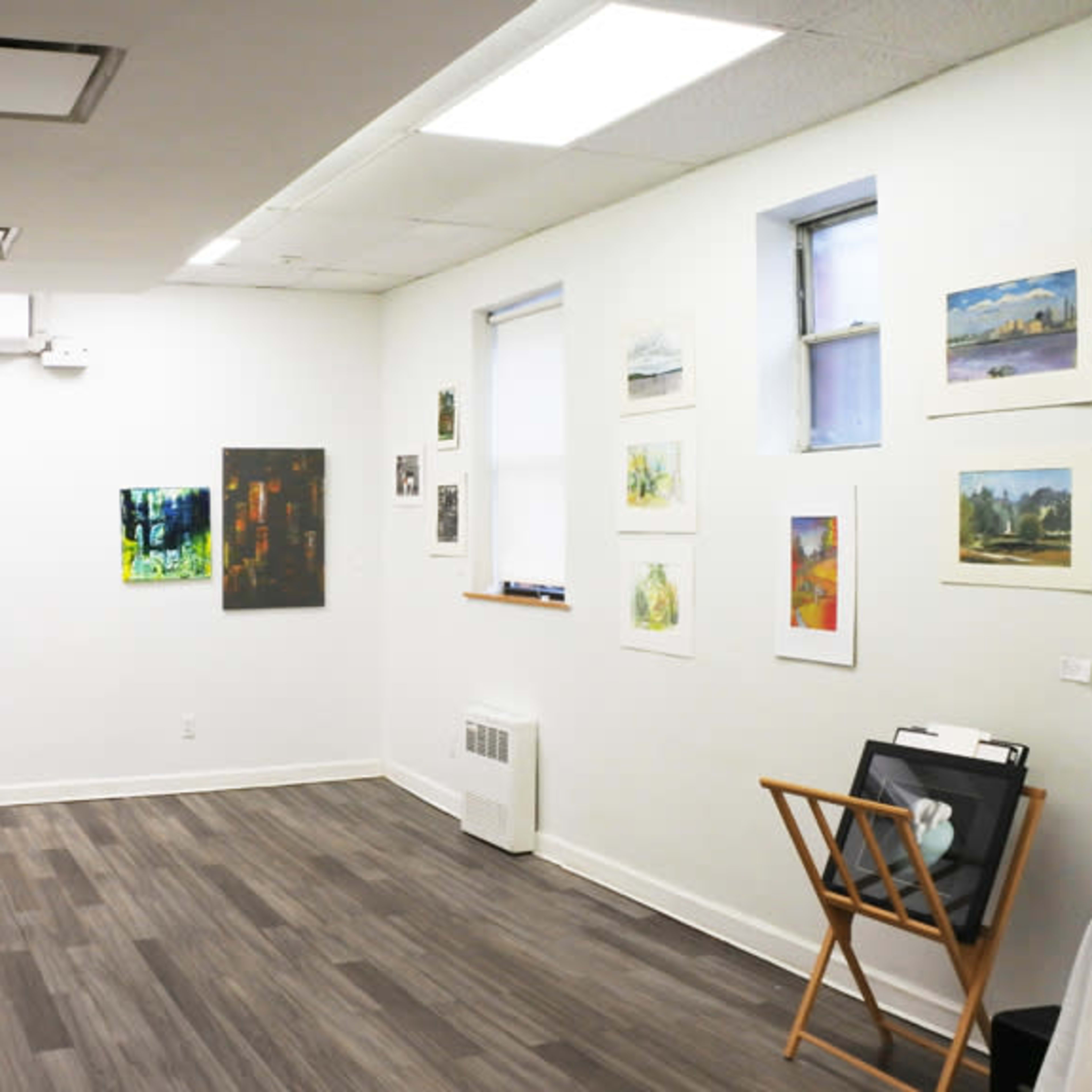 An art gallery with various paintings and artworks displayed on the walls and a folding chair in the corner.