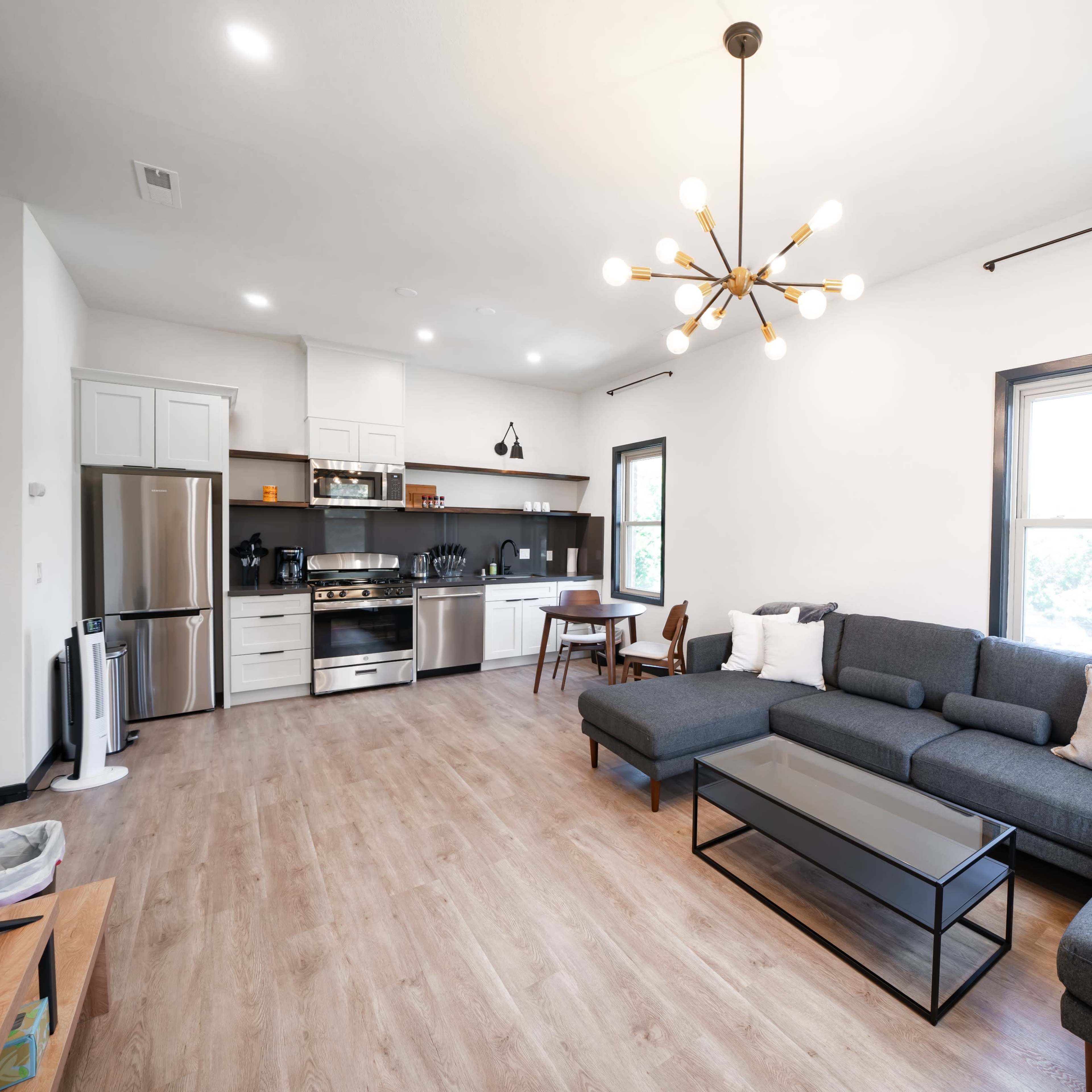 A modern living room with a sectional sofa, a coffee table, and a kitchen area featuring stainless steel appliances.