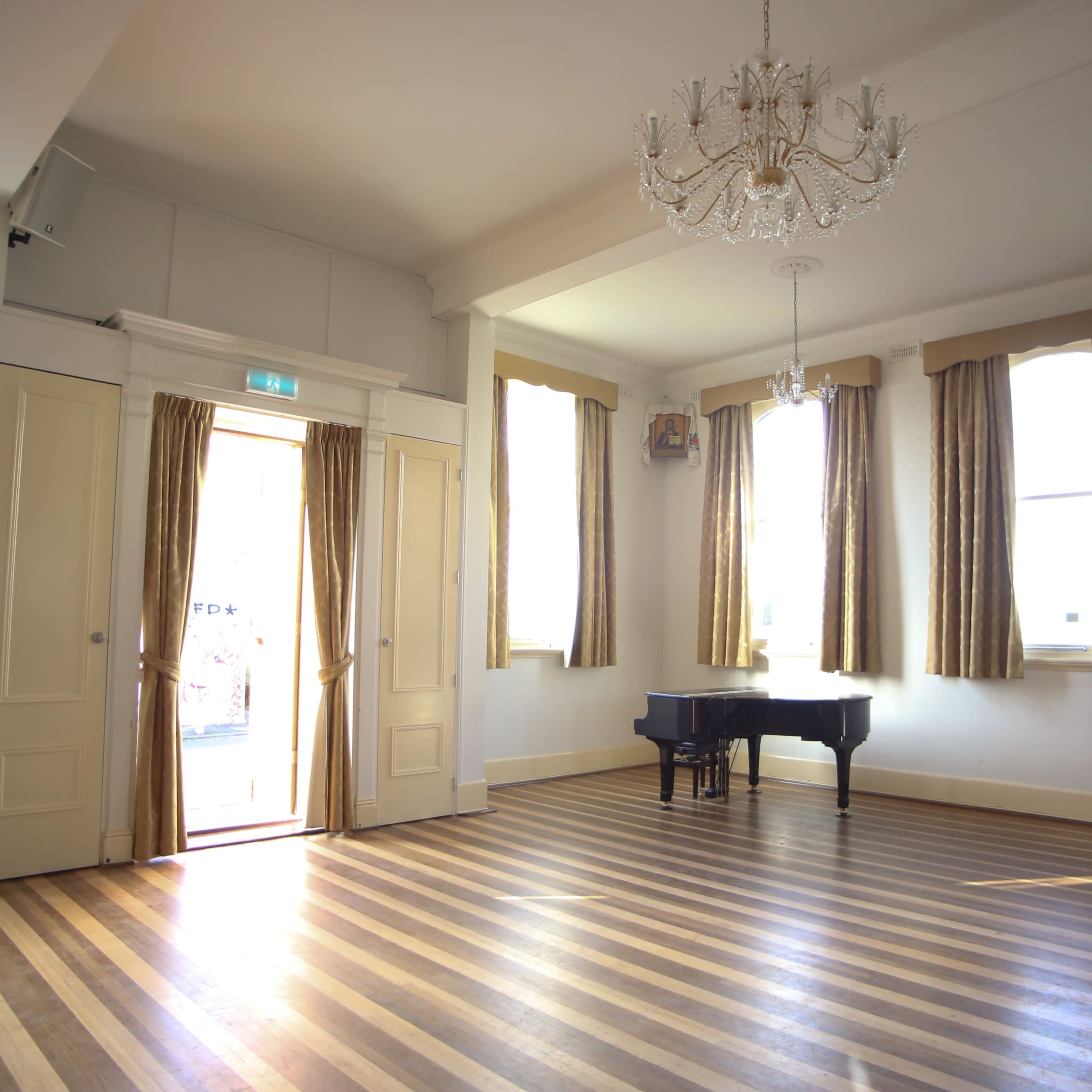 A spacious room with a grand piano, wooden striped flooring, and tall windows dressed with curtains.