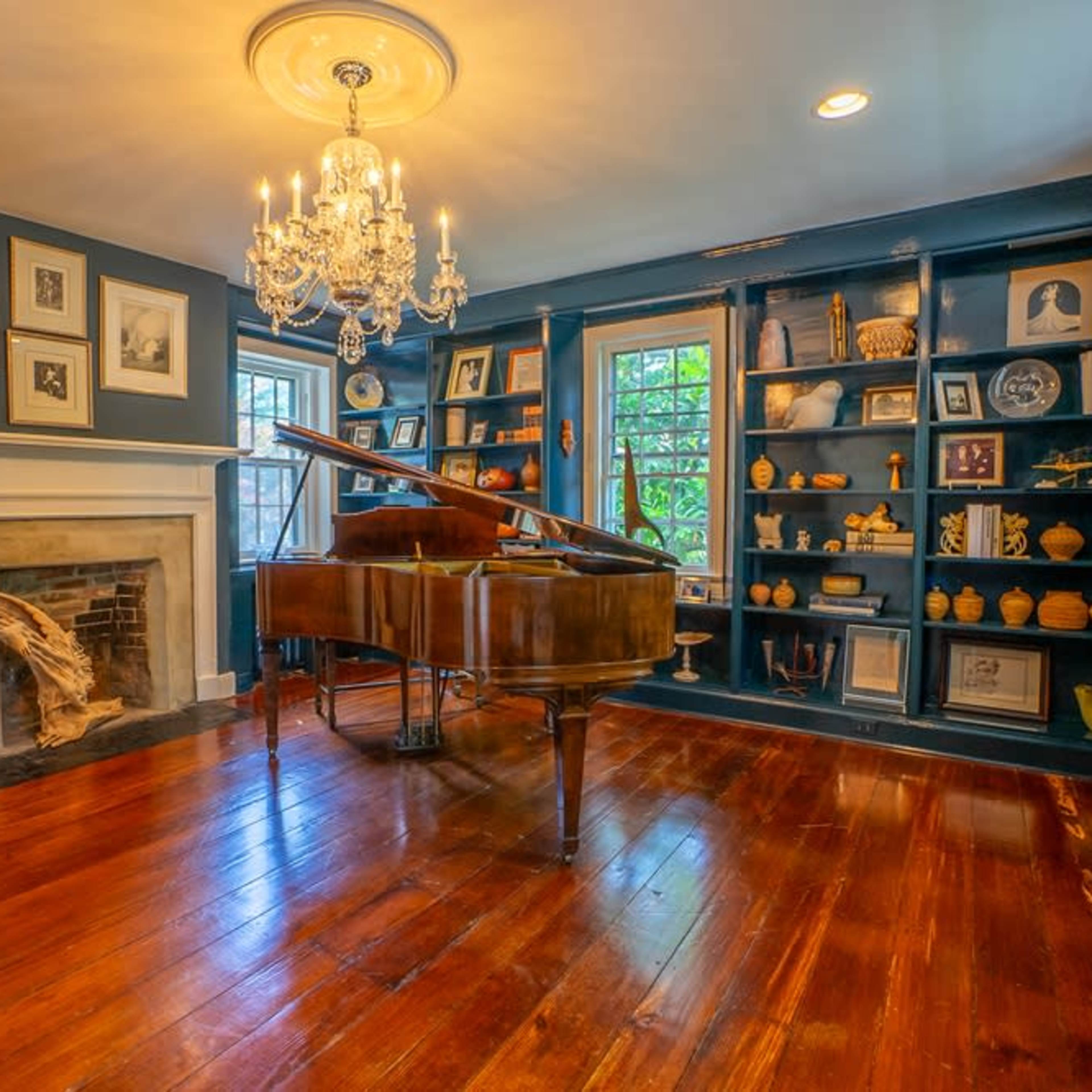 A grand piano is positioned in the center of a room with blue walls, a fireplace, and built-in shelves lined with decorative items.