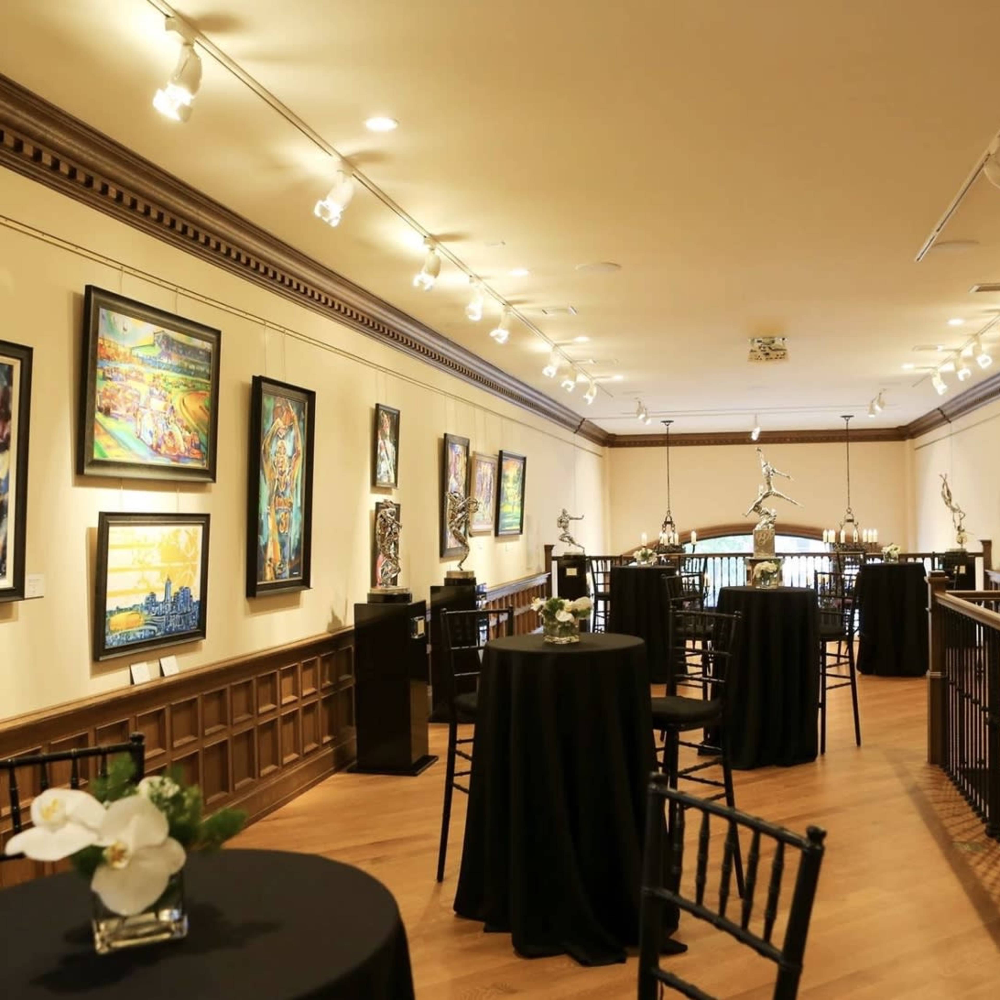 An art gallery with framed paintings displayed on the walls and small tables arranged throughout the space.