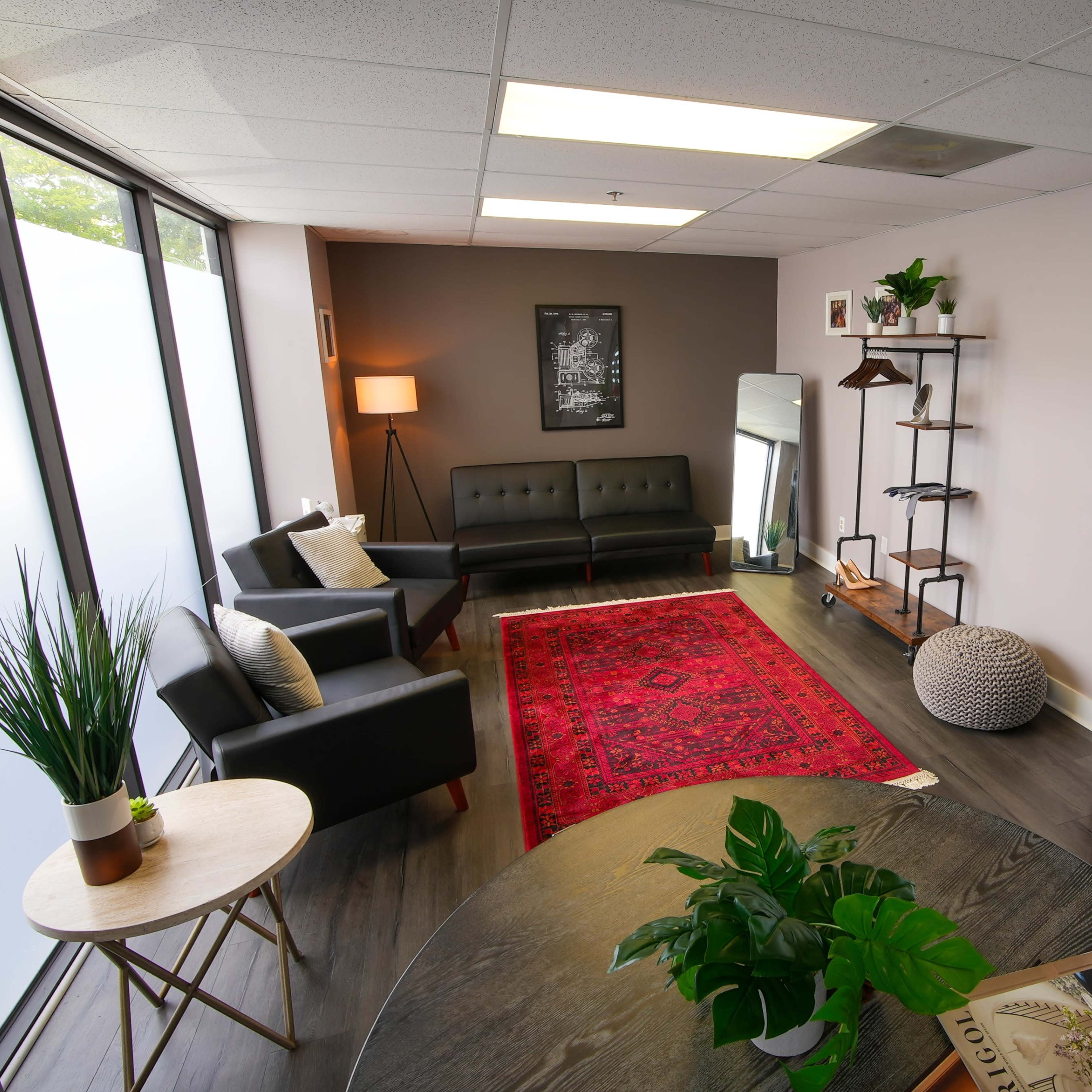A modern interior of a well-lit room featuring a seating area with a sofa, a round table, a mirror with lights, and decorative plants.
