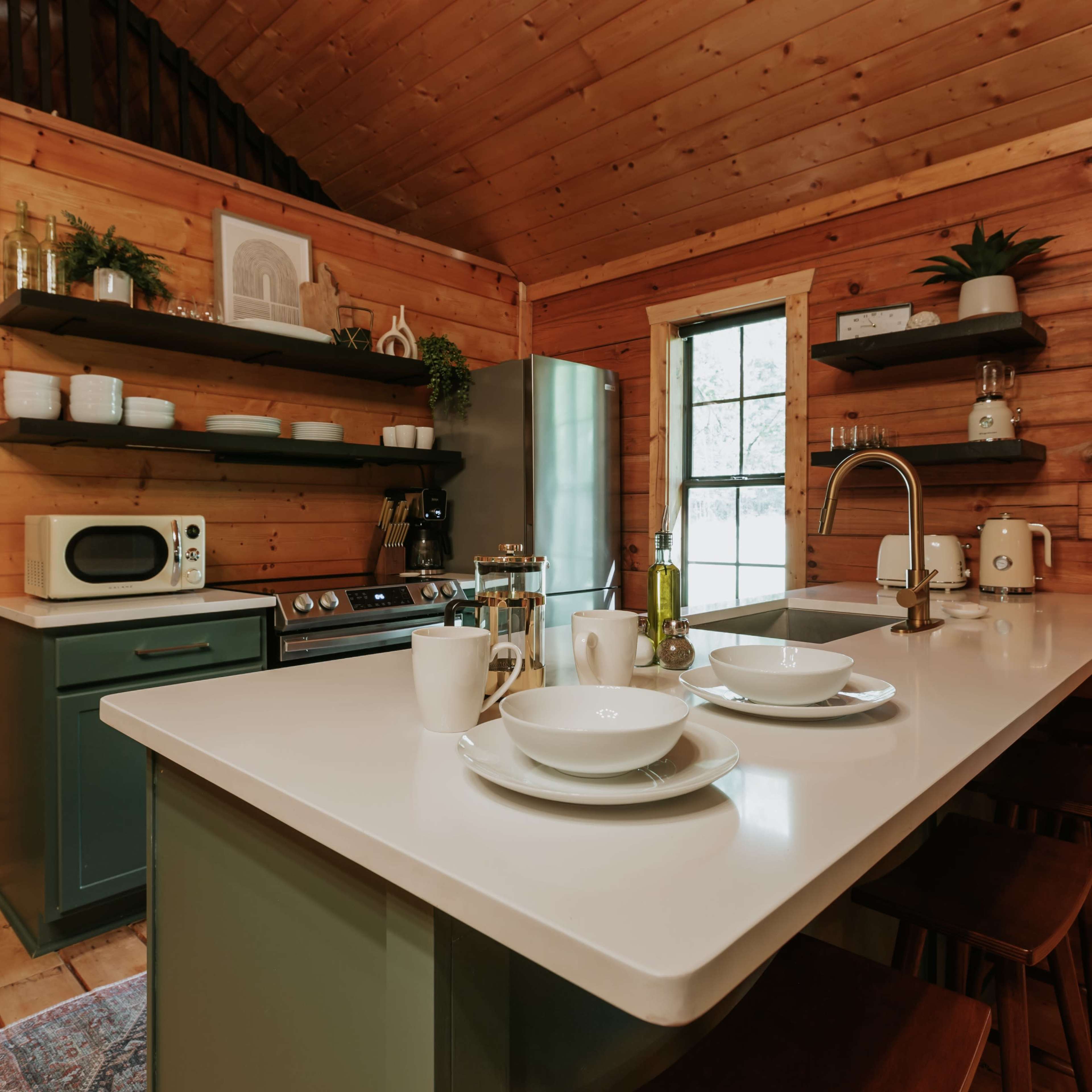A rustic kitchen with wooden walls, a modern island with tableware, and shelves displaying kitchen items.