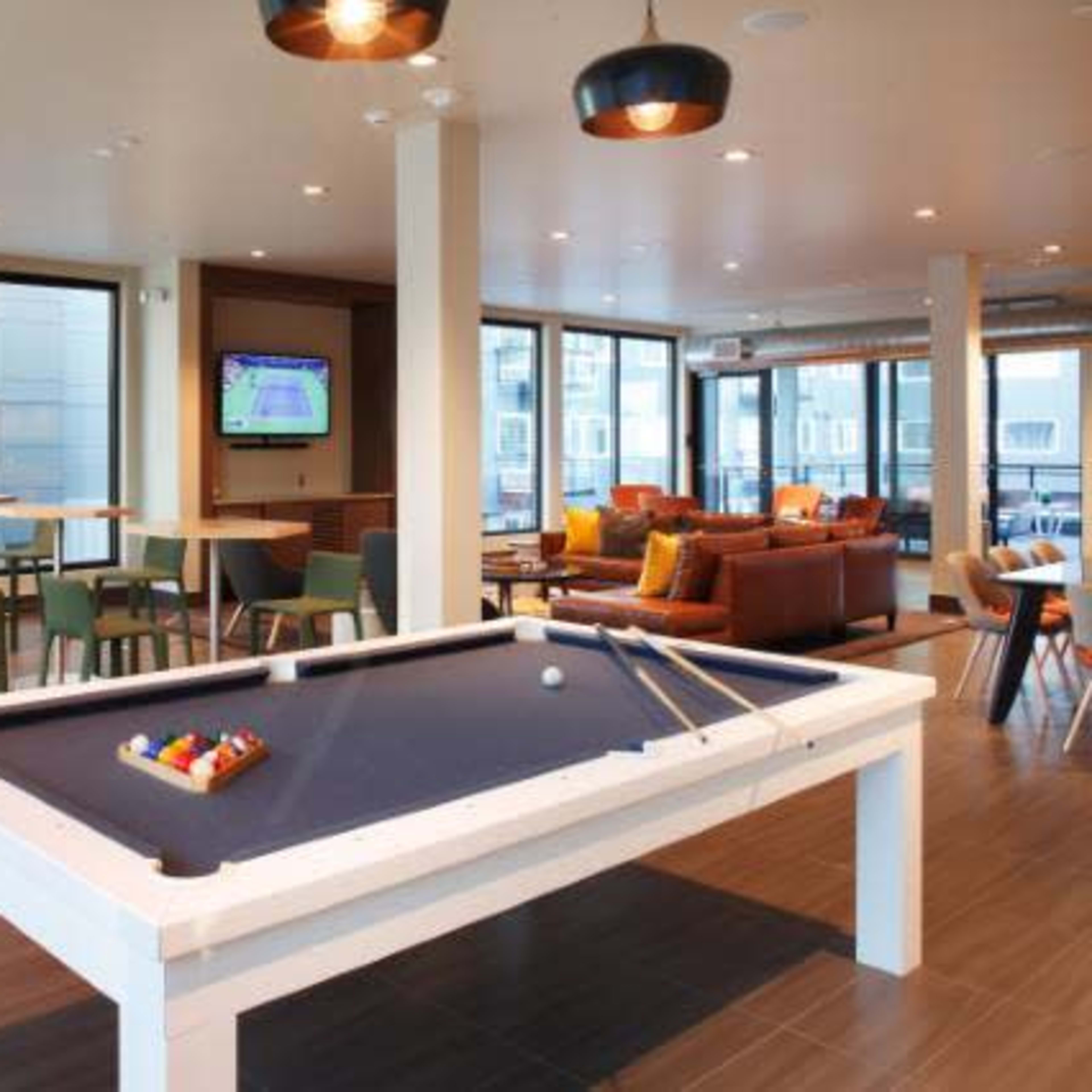 A modern recreational room featuring two billiard tables, a seating area with a couch and chairs, and a television mounted on the wall.