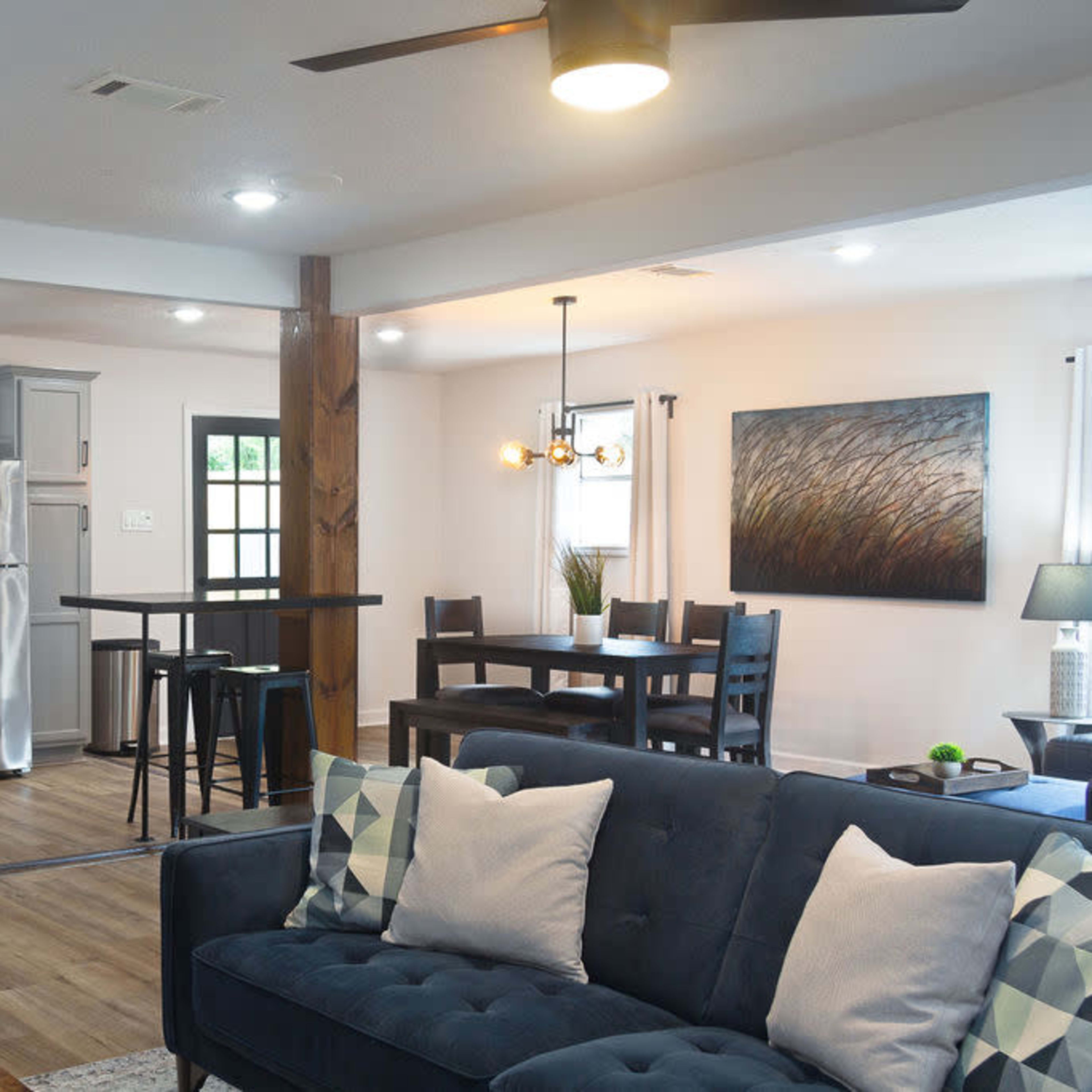 A modern open-concept living space with a kitchen, dining area, and seating area featuring a blue sofa and wooden accents.