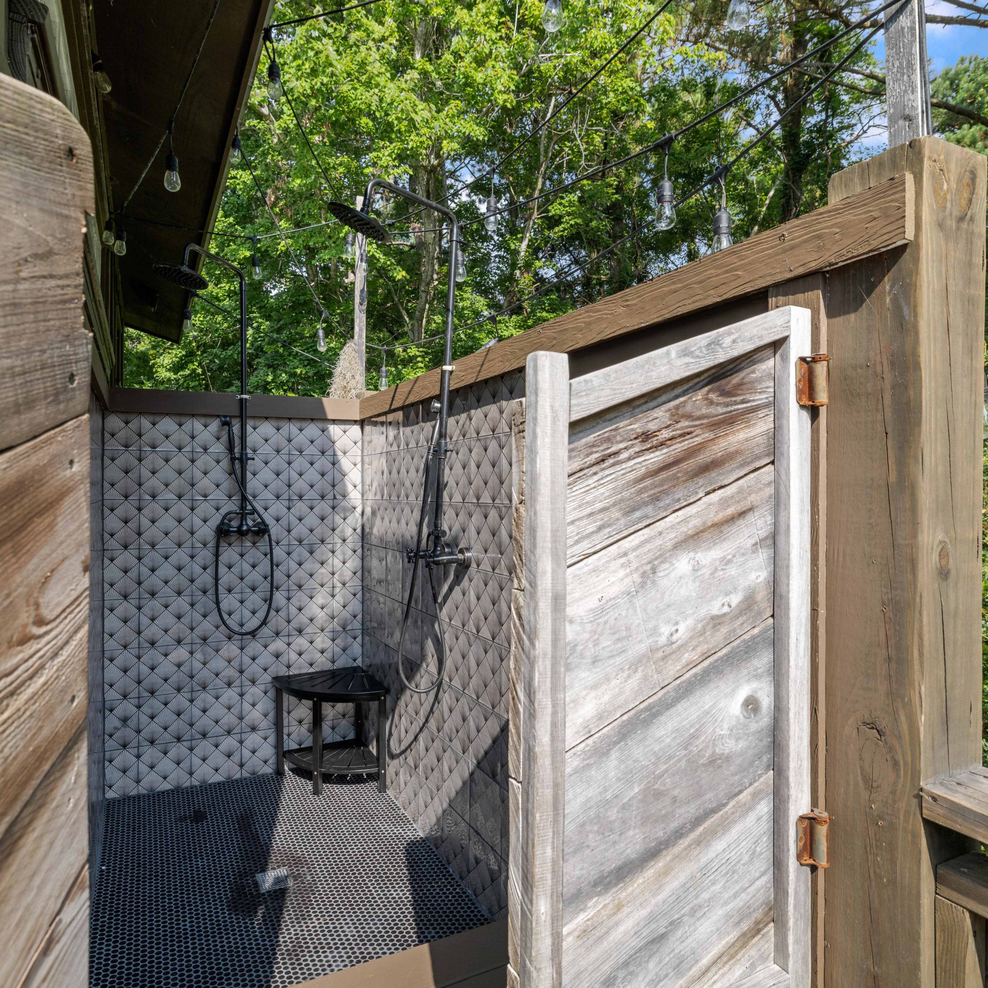 An outdoor shower with a wooden enclosure, featuring a textured tiled interior and a stool.