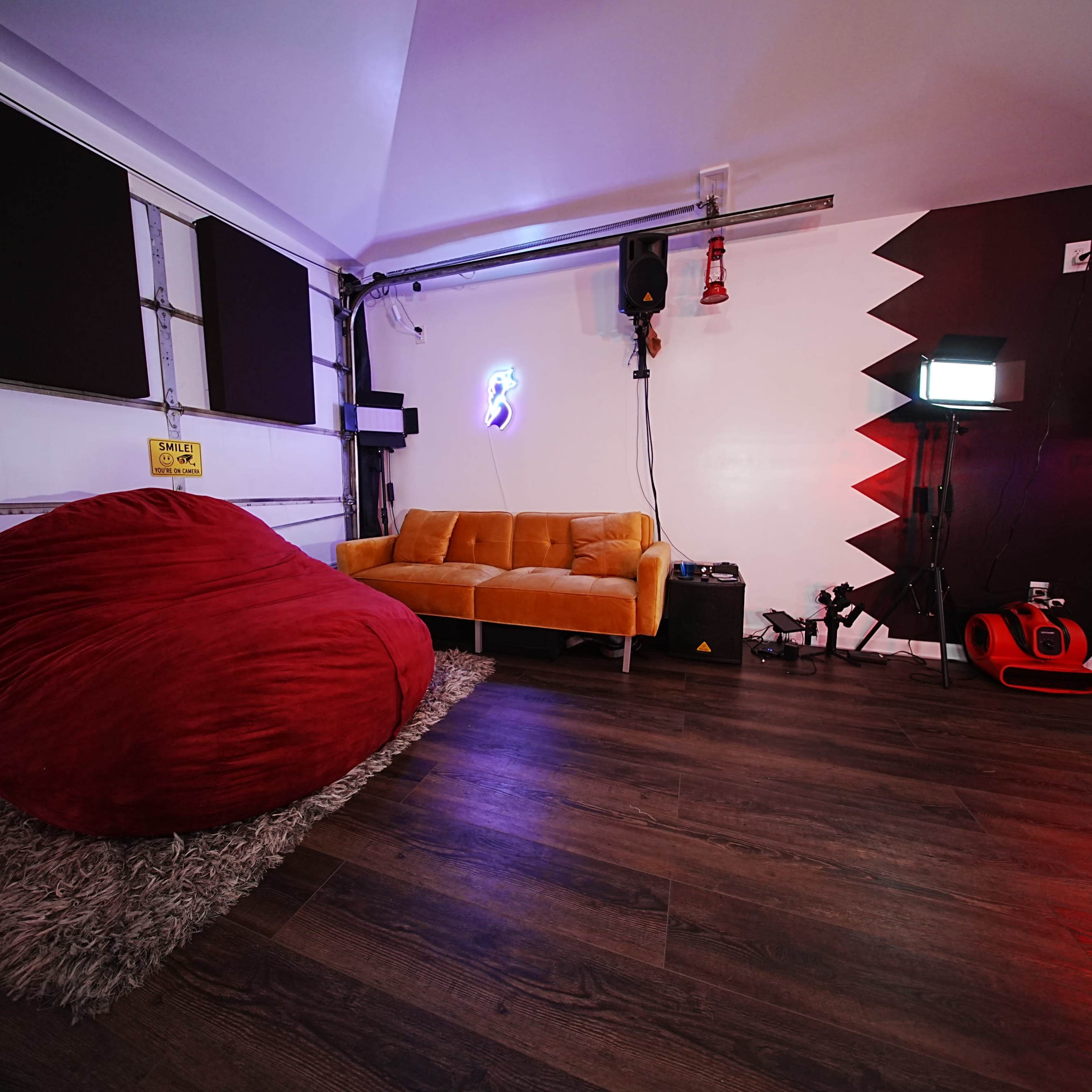 A room featuring a large red bean bag chair, a yellow couch, and various lighting equipment in a modern setting.