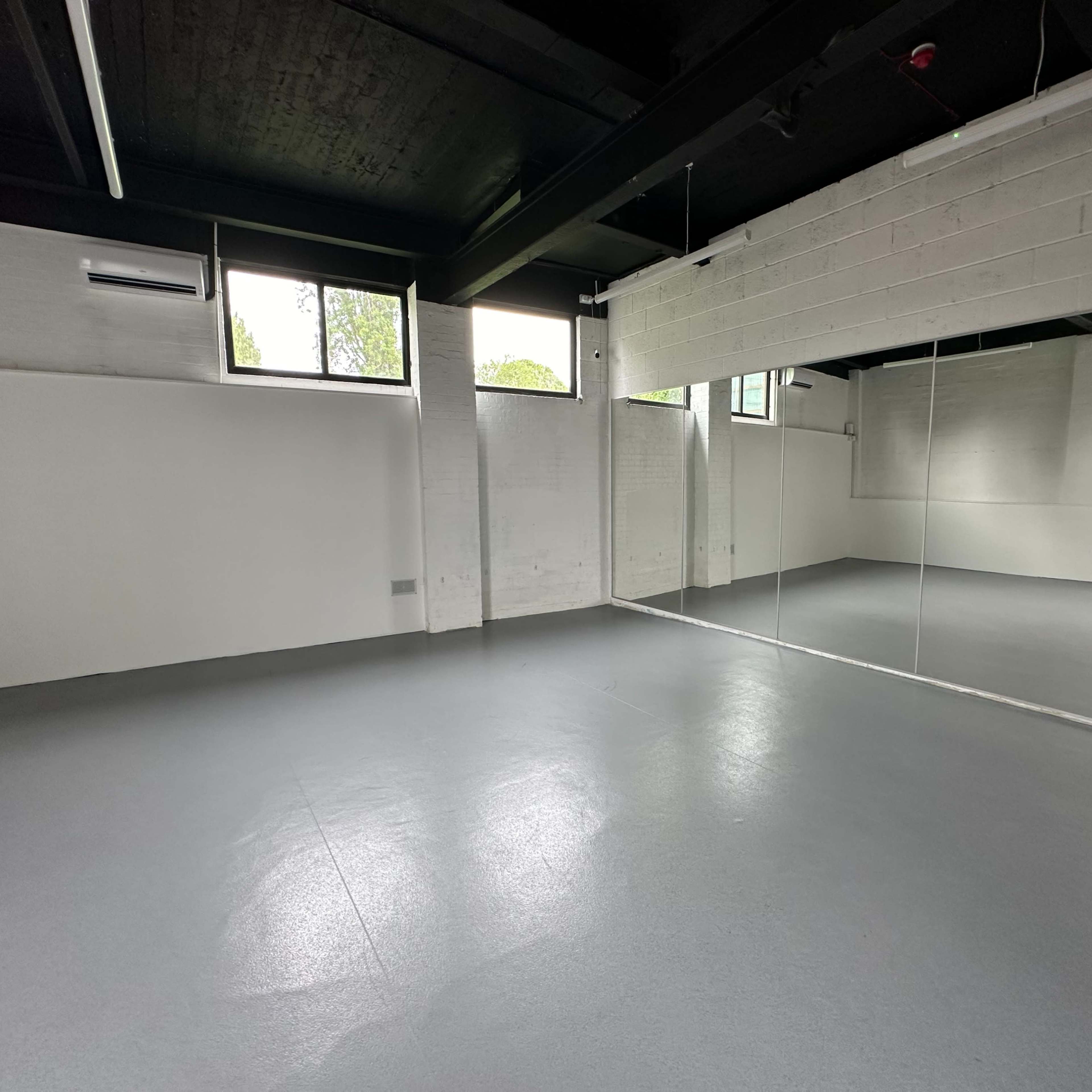 A spacious, empty room with gray flooring, white walls, and large mirrors along one side.