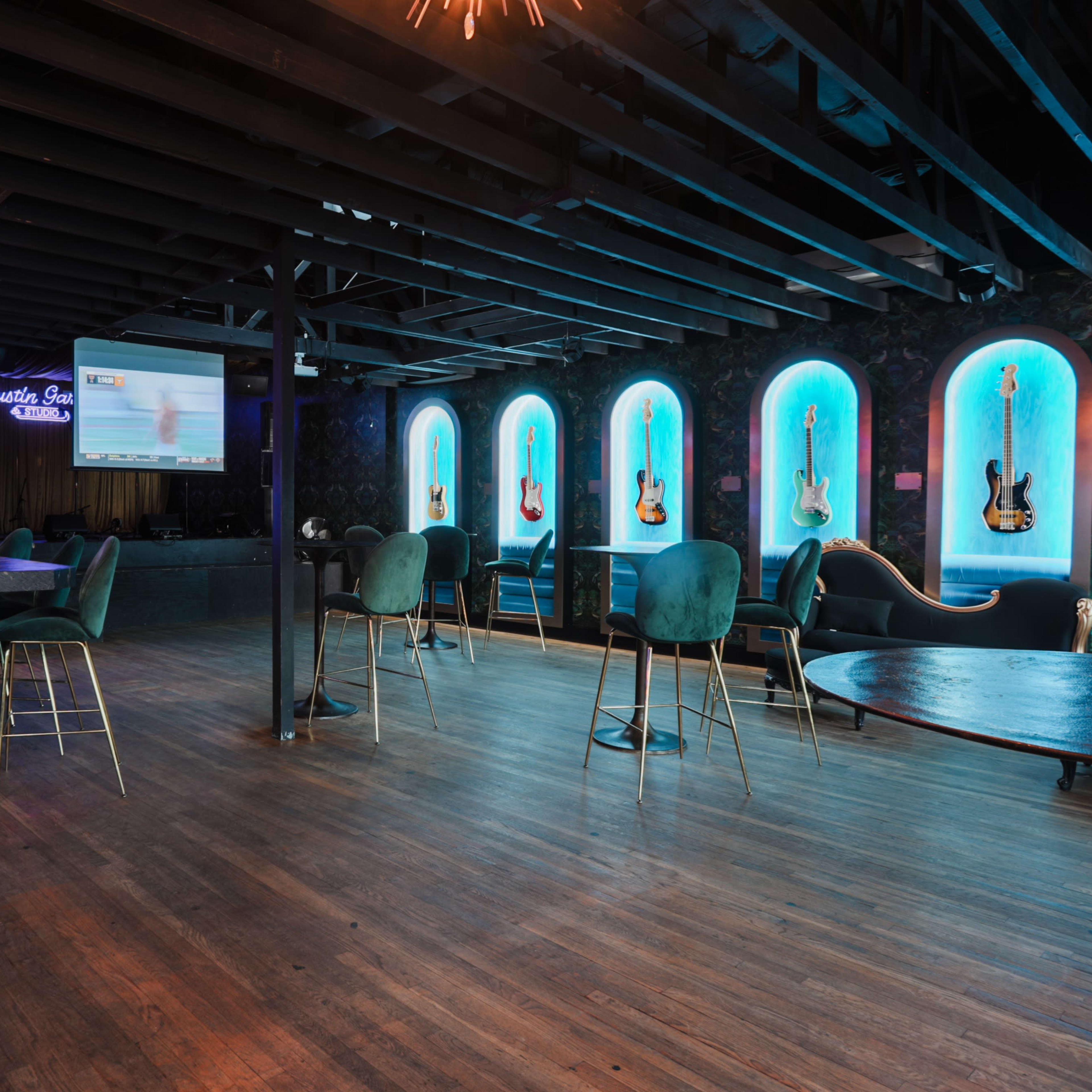 A spacious bar interior features a wooden floor, illuminated blue archways showcasing guitars, and seating arranged around low tables.