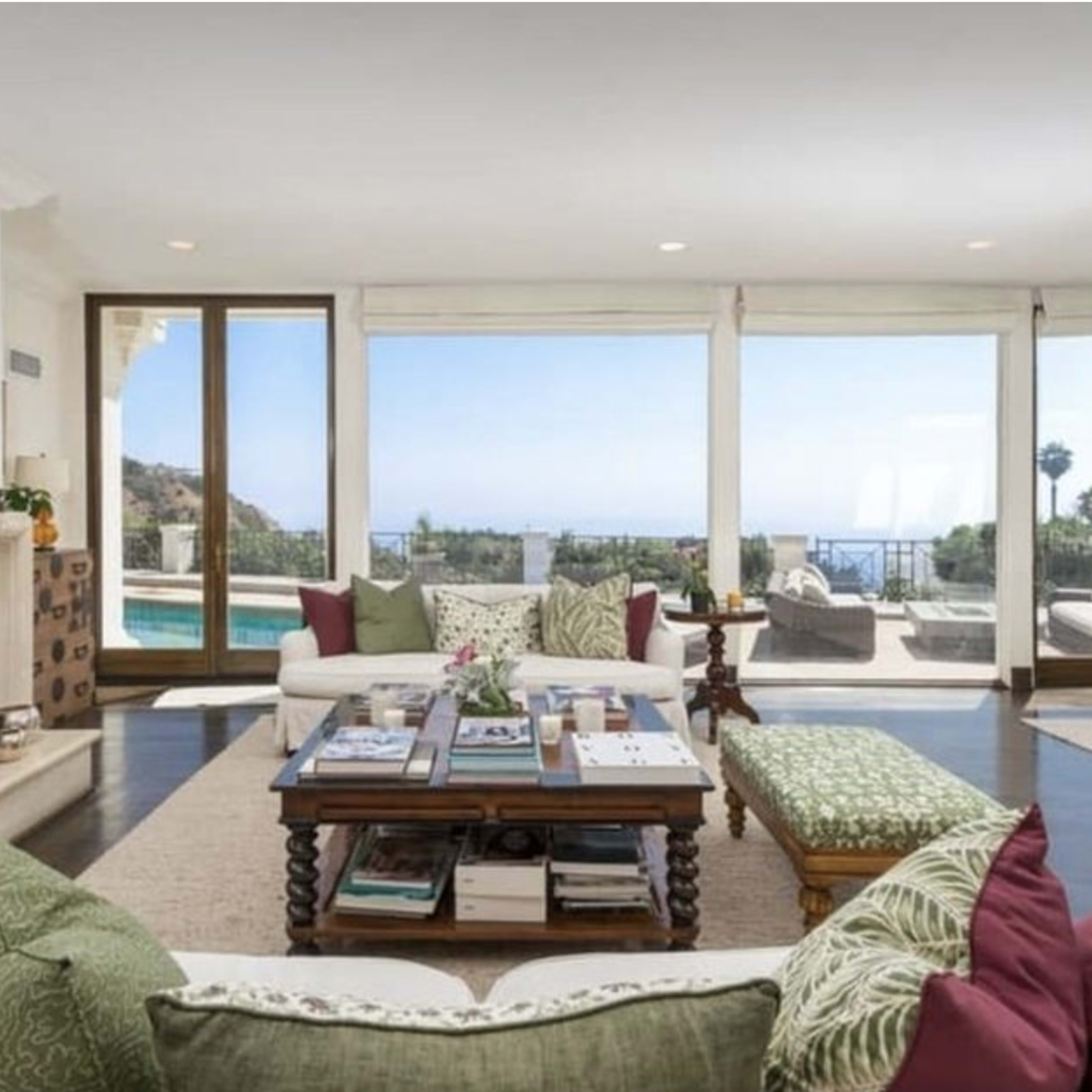 The living room features a cozy seating area with a coffee table, large windows showcasing a view of the pool and outdoor scenery.