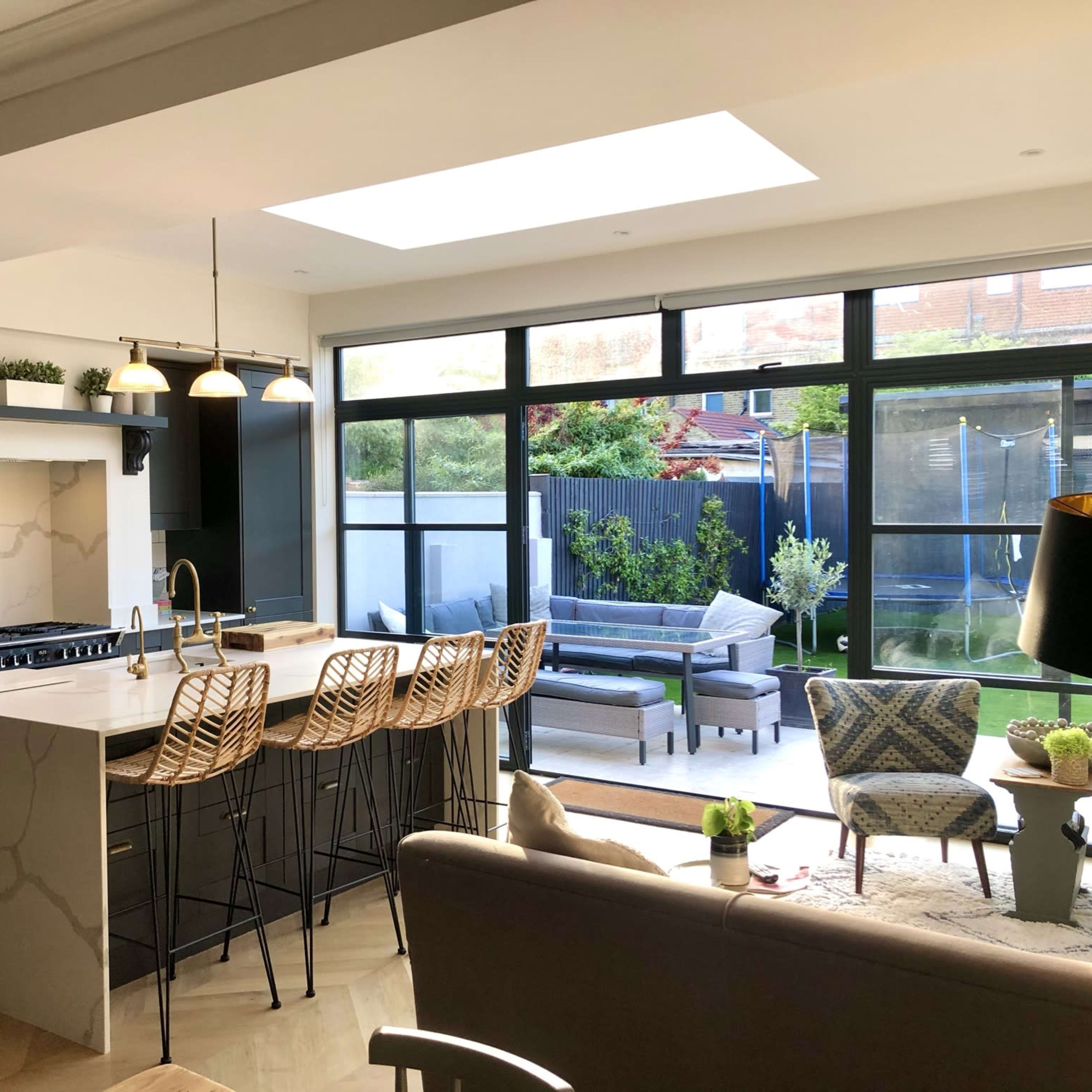 A modern kitchen features a large island with bar stools, open shelving, and a view of an outdoor seating area through large glass doors.