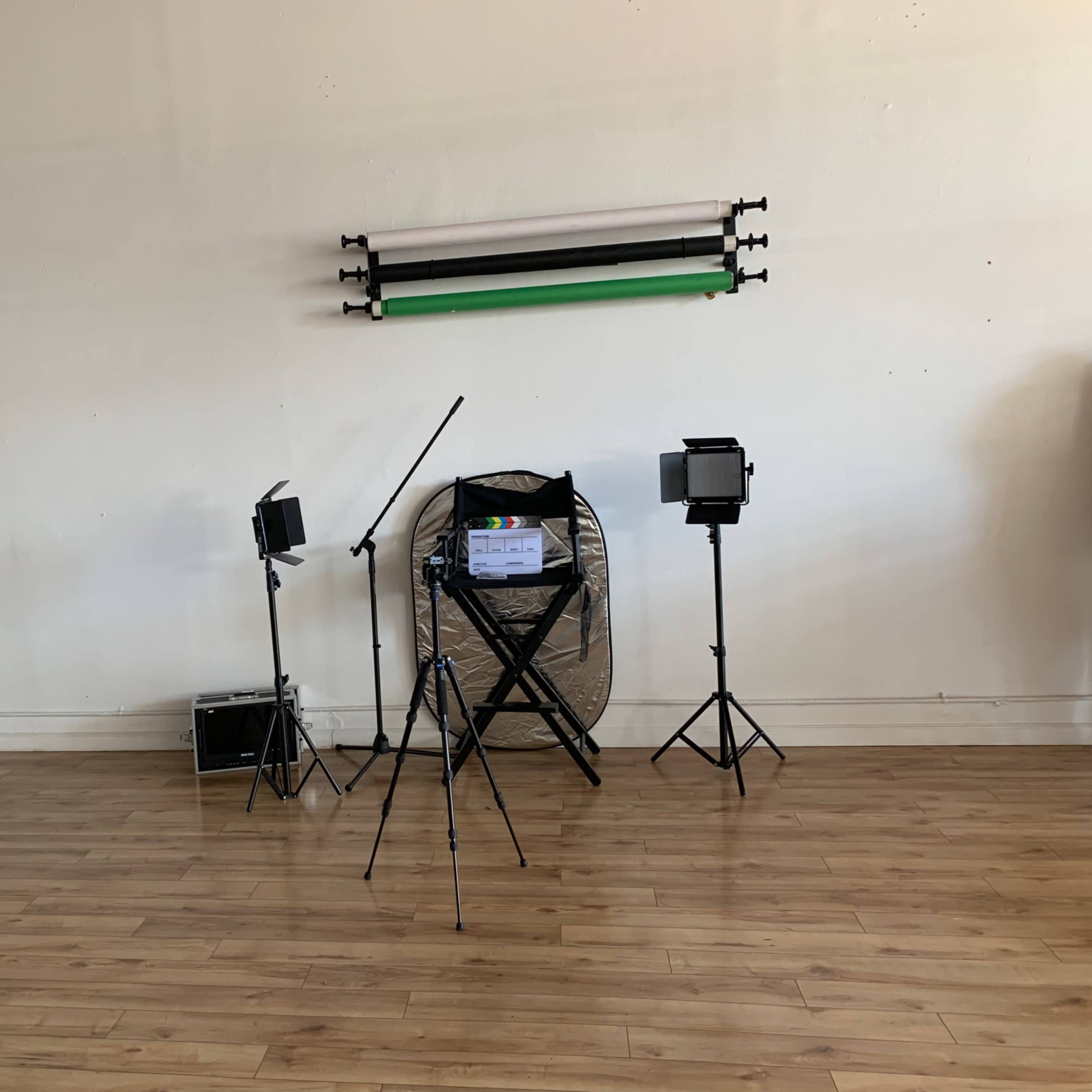 A photography studio with two light stands, a fan, a director's chair, and backdrop support rods mounted on the wall.