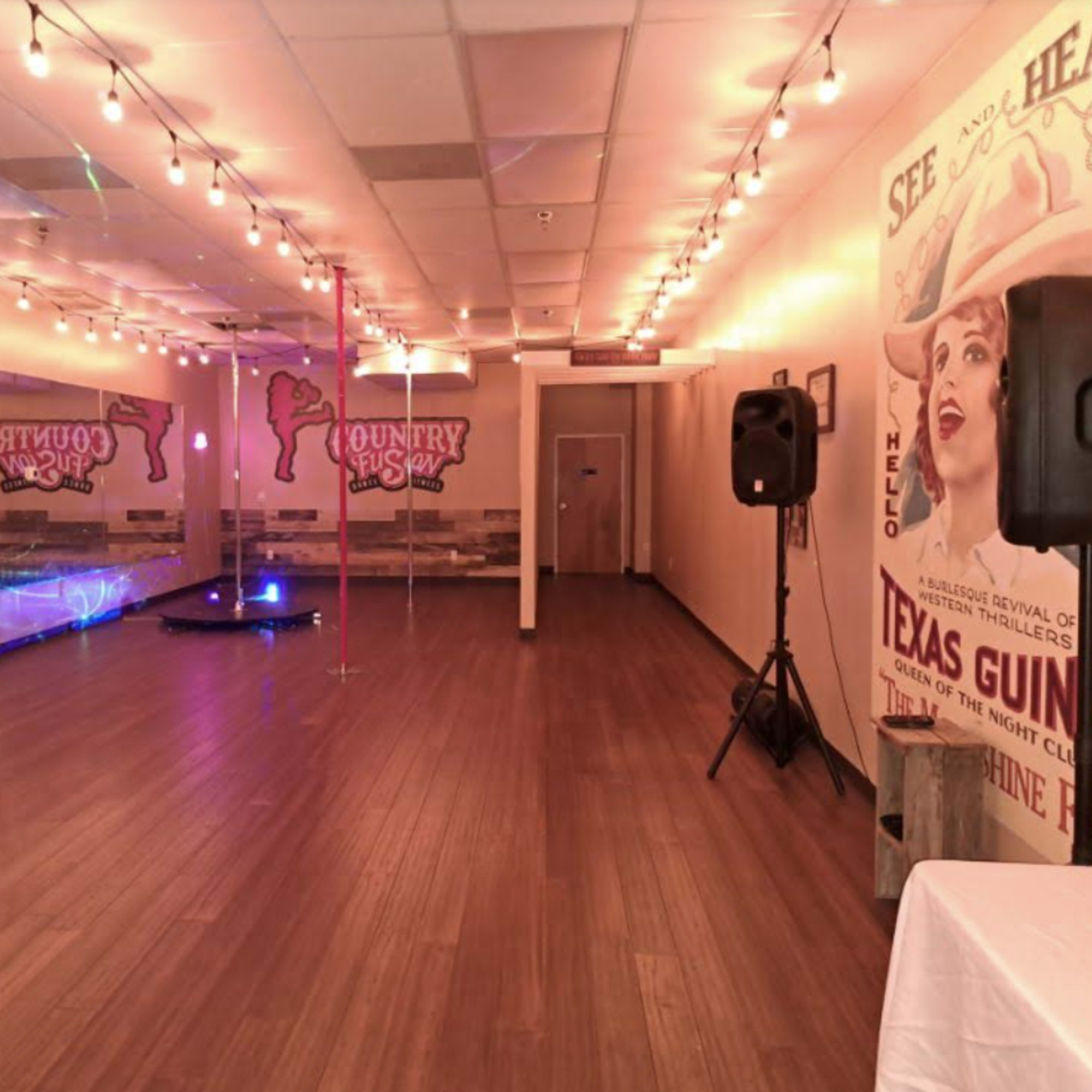 A spacious dance studio with wooden flooring, a mirrored wall, and colorful lighting in a setting decorated with vintage-style posters.