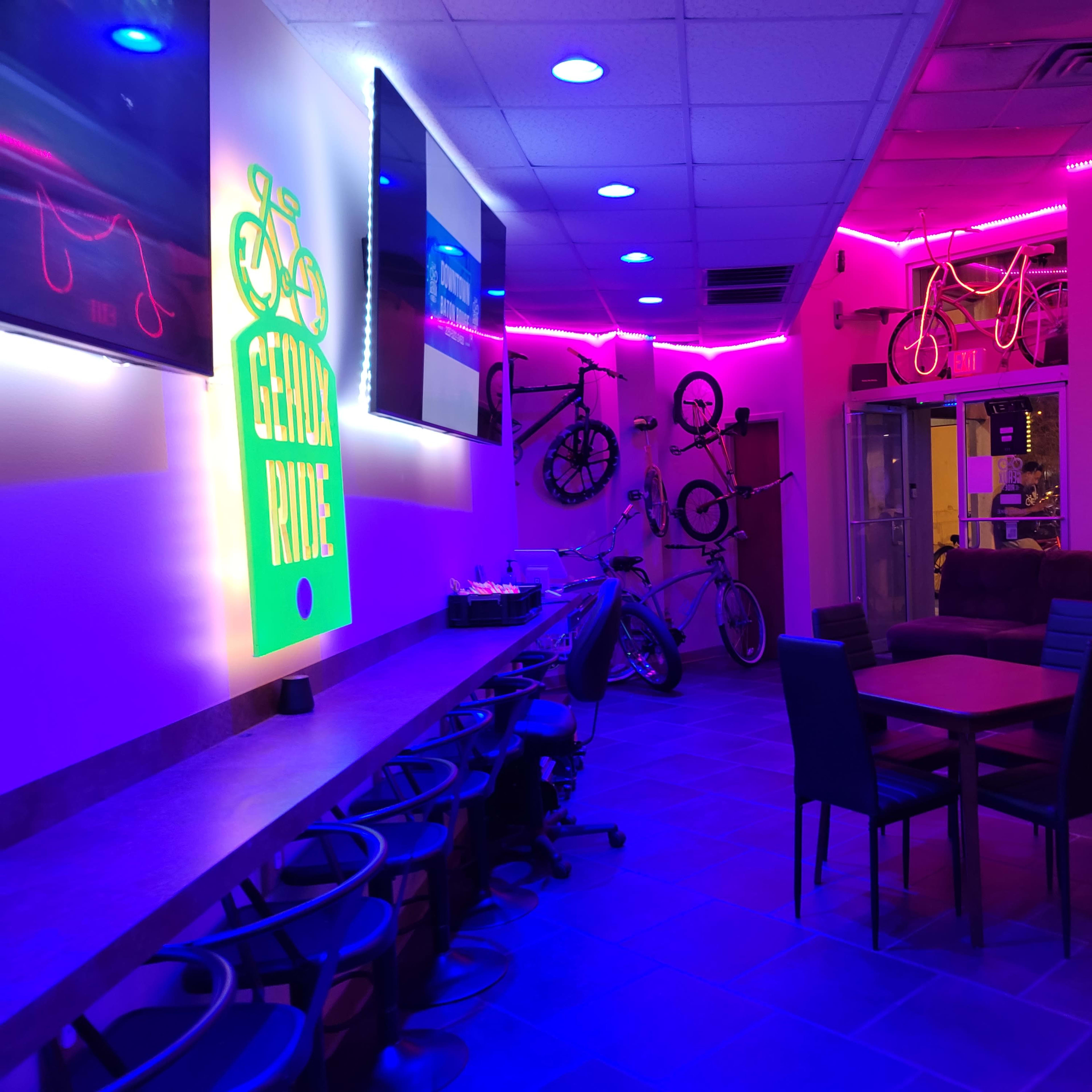 A brightly lit bicycle-themed café with neon lights, bicycle decorations on the walls, and seating areas.