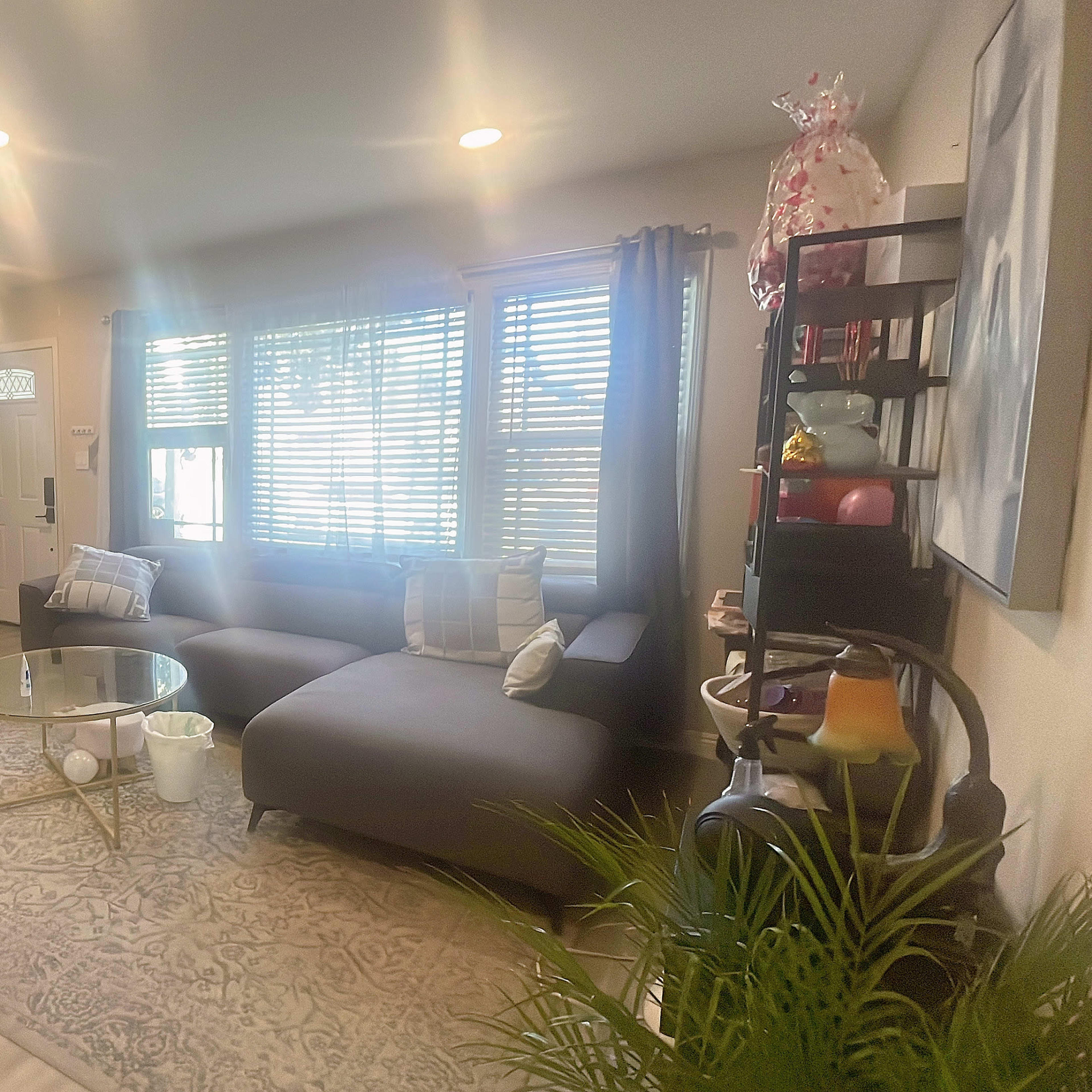 A modern living room with a gray couch, a round coffee table, and large windows allowing natural light to enter.