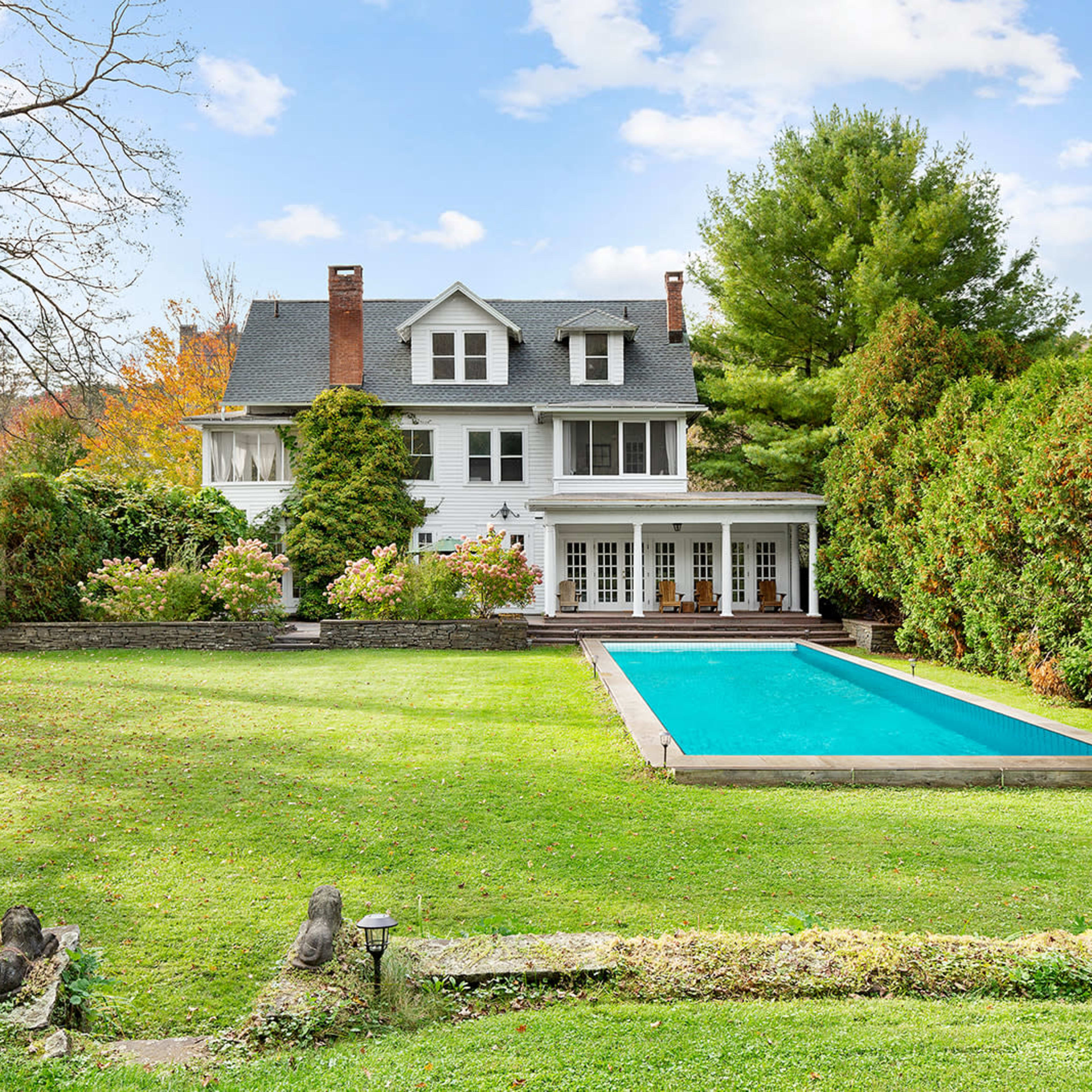 A large house with multiple stories is situated in a backyard featuring a swimming pool and well-maintained greenery.