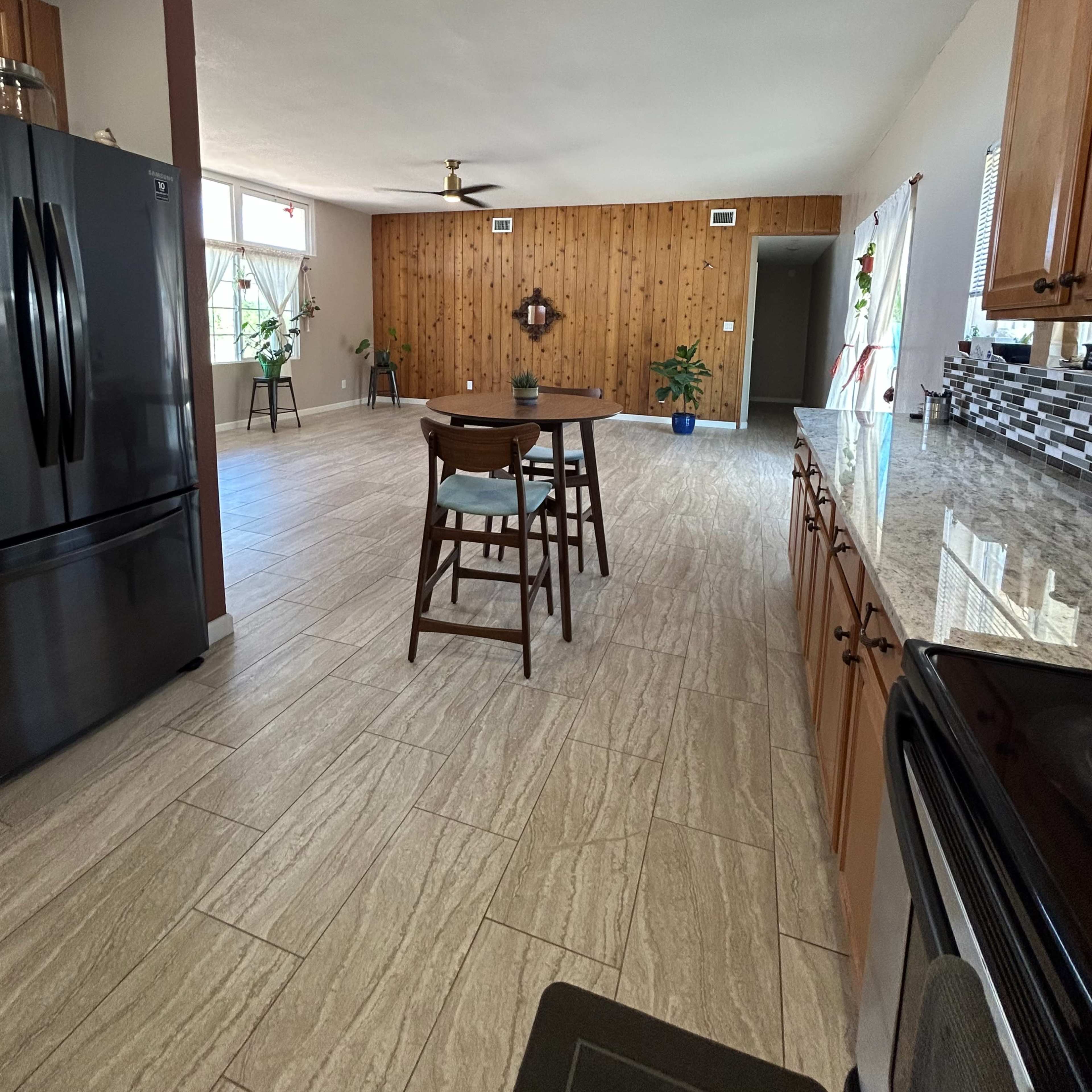 A spacious kitchen features wooden paneling, granite countertops, a black refrigerator, and a central table with chairs.