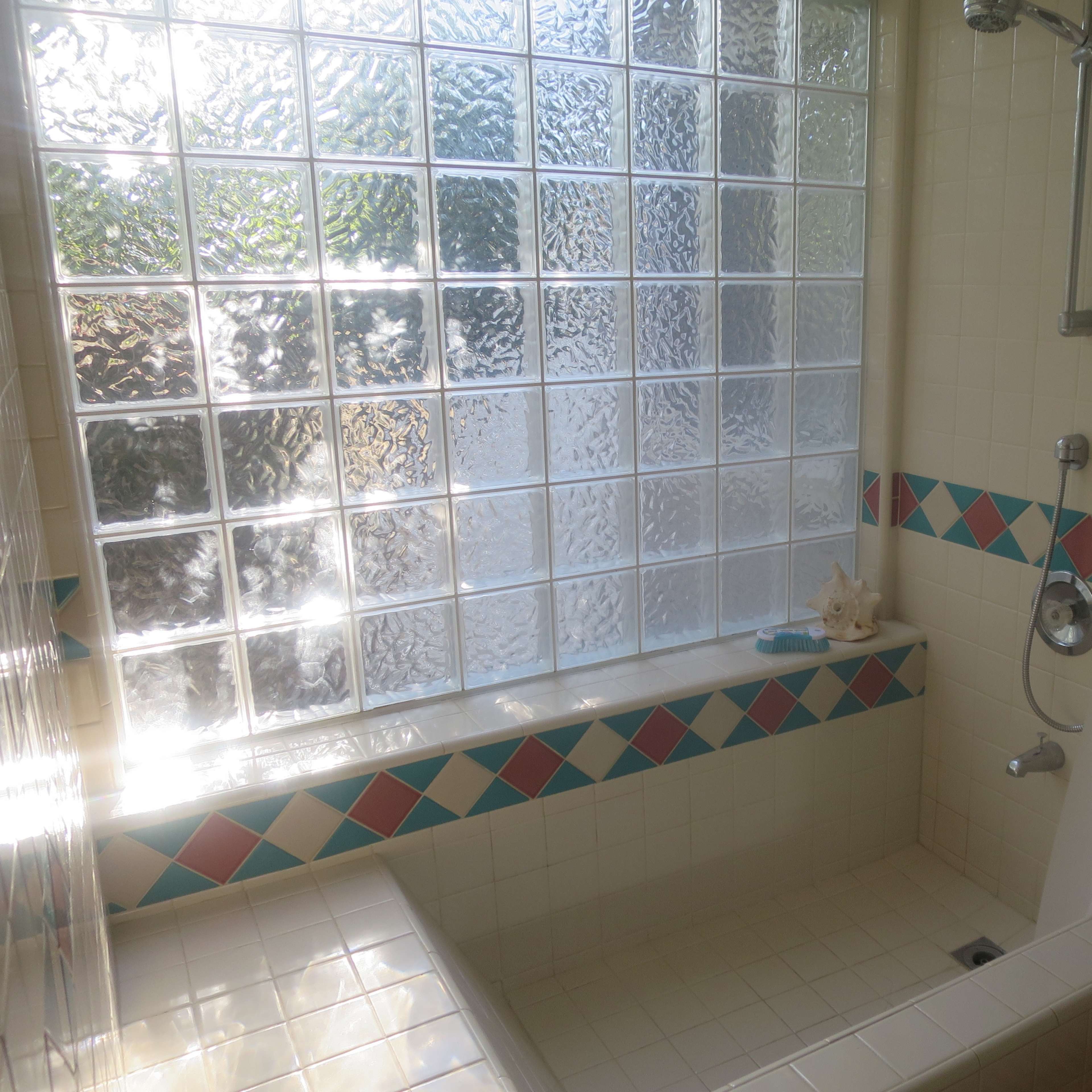 A bathroom with a shower area featuring a glass block window, tiled walls with diamond patterns, and a bathtub.