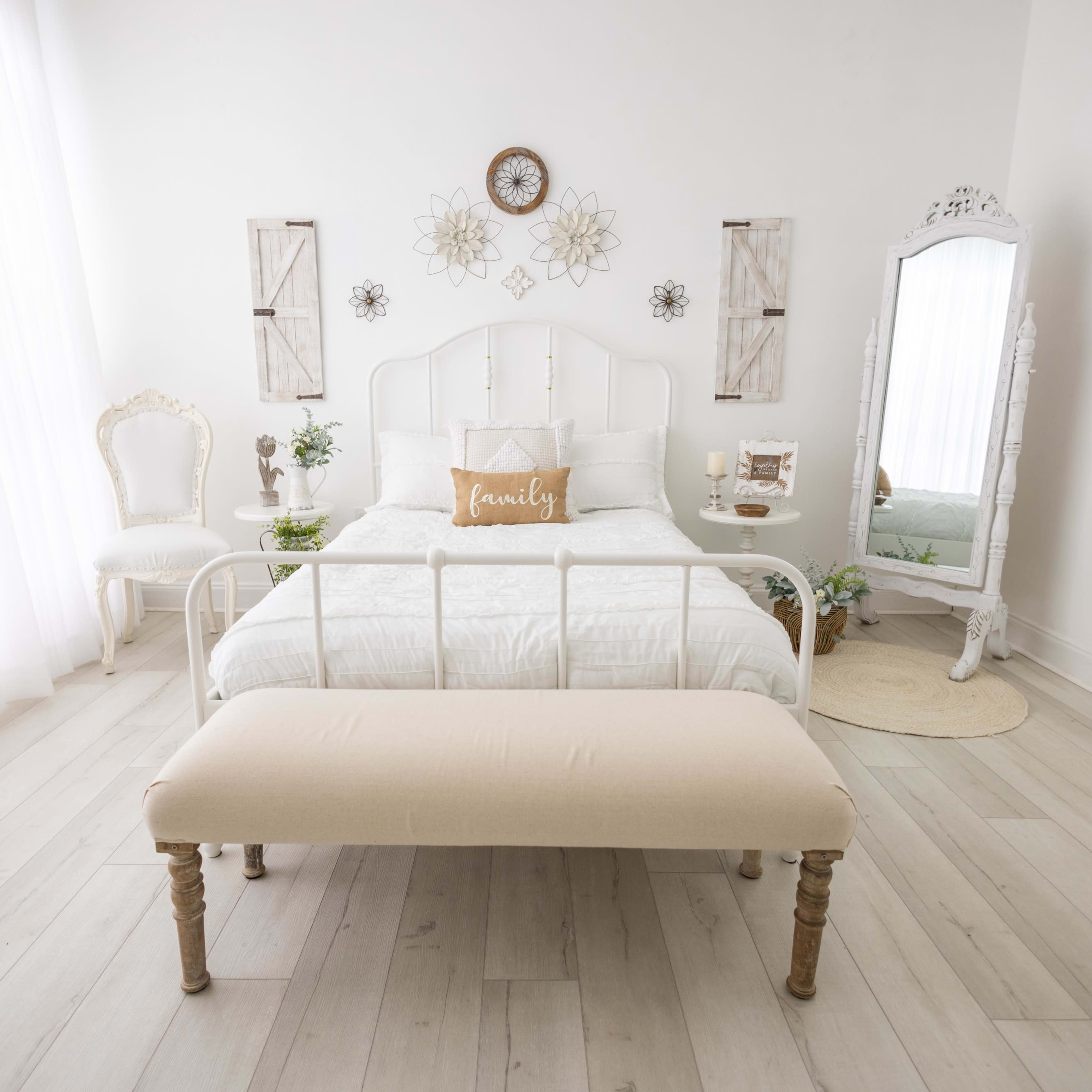 A bright, modern bedroom with a white metal bed, light wooden floors, and a decorative mirror.
