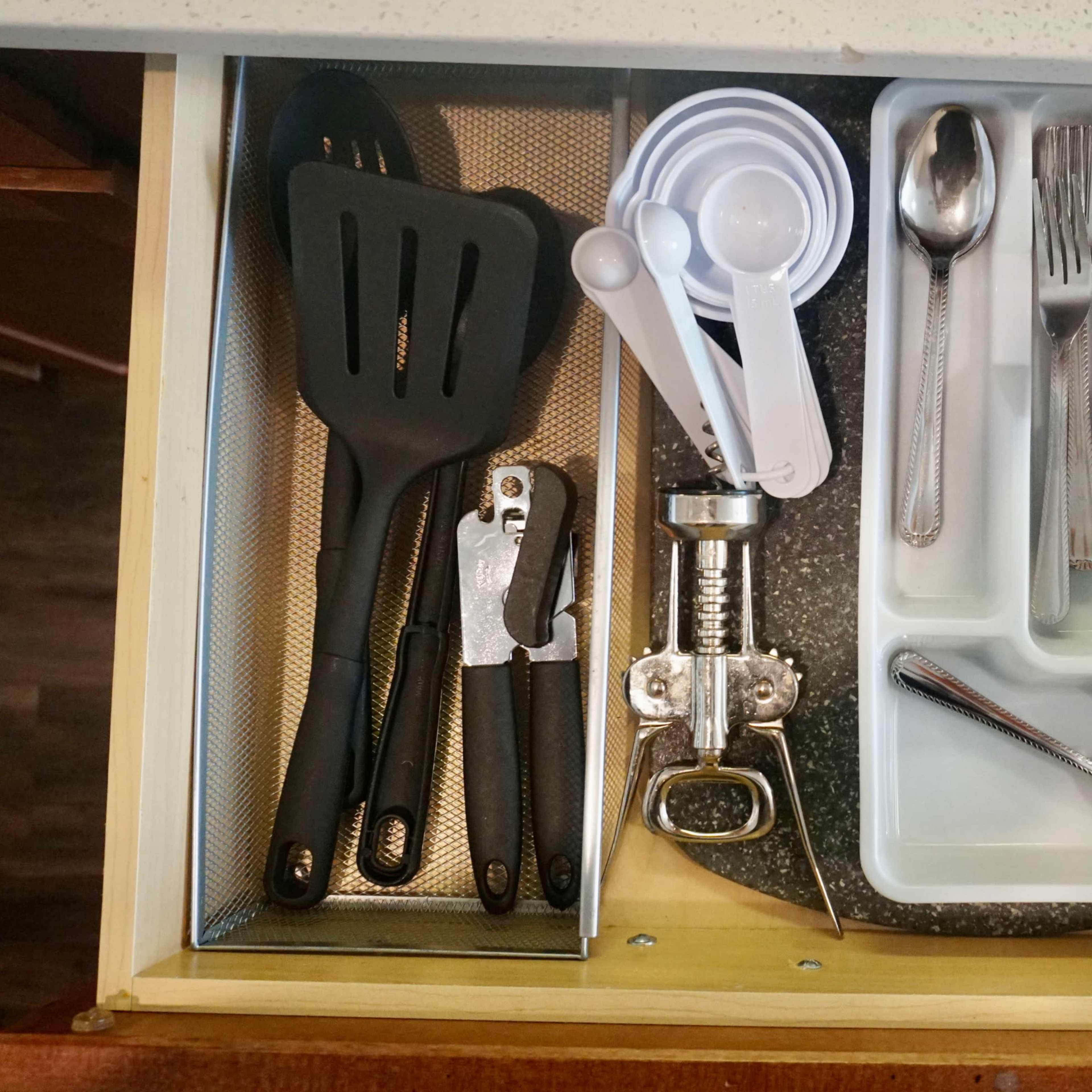A kitchen drawer organized with various utensils, including spatulas, a can opener, measuring cups, and cutlery.