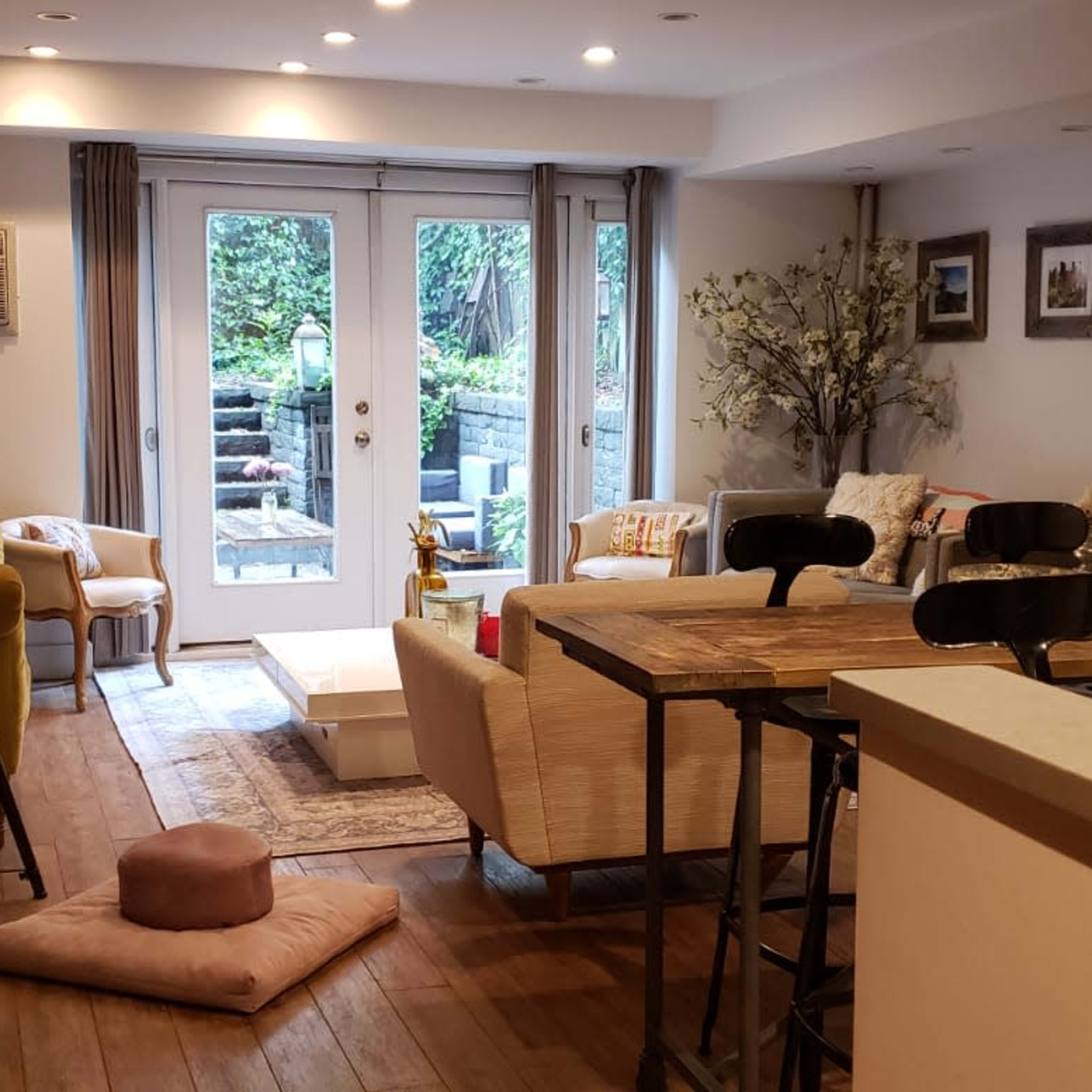 A cozy living room with wooden flooring, featuring a seating area, a dining table, and access to a garden through sliding glass doors.