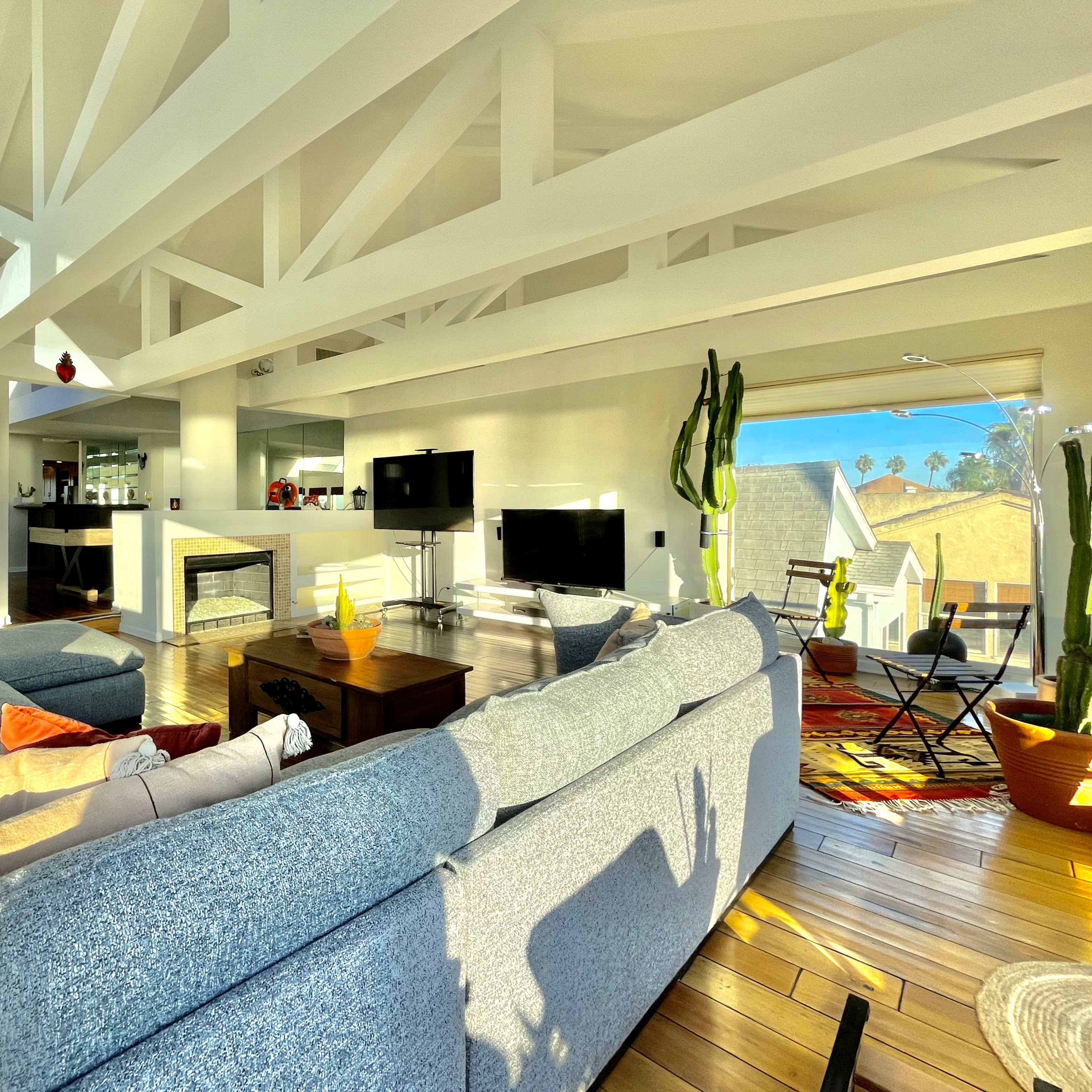 A modern living room with large windows, a fireplace, and comfortable seating arranged around a central coffee table.