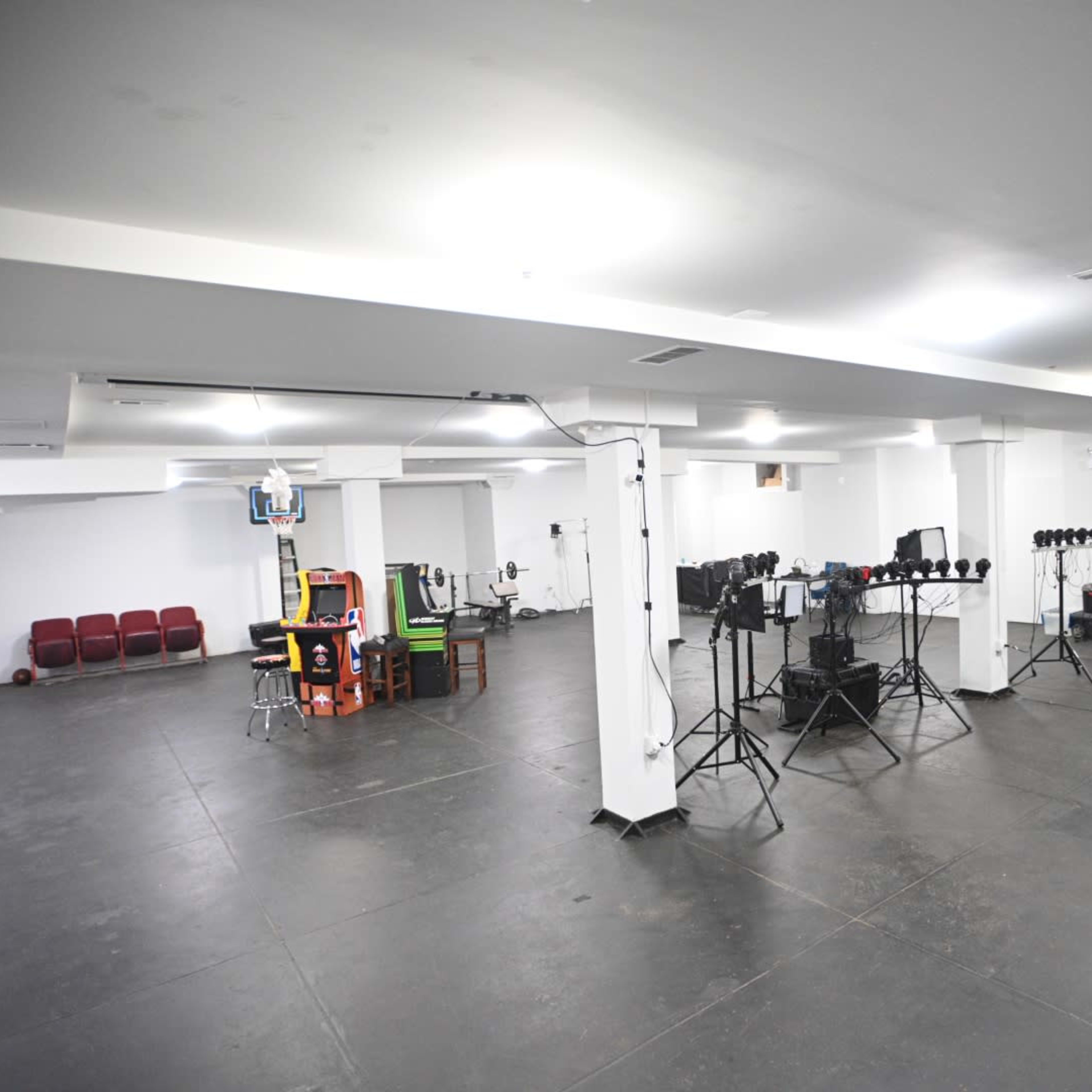 A spacious studio with various lighting equipment, a basketball hoop, and a setup for seating and filming.