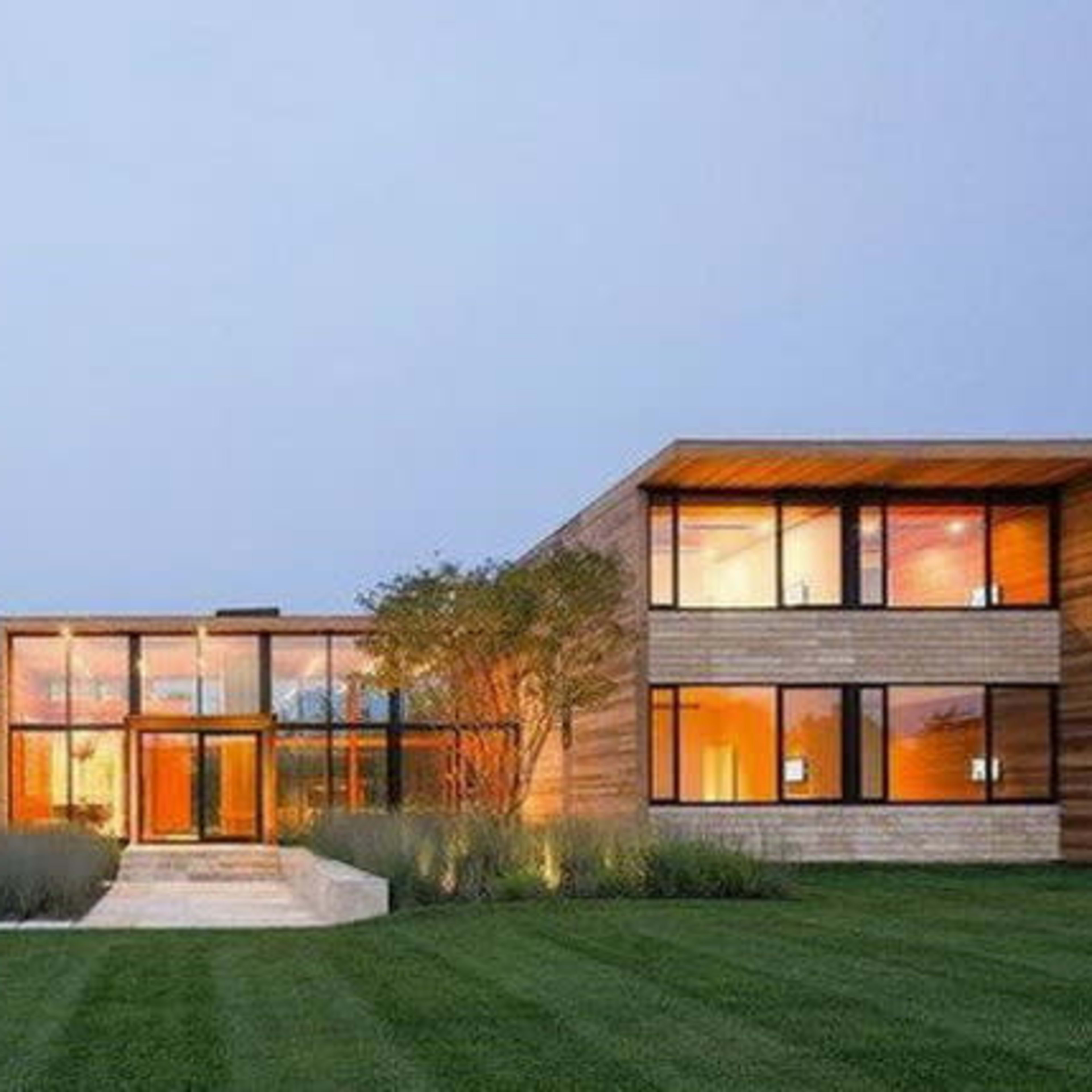 A modern house features large glass windows, wooden accents, and a neatly landscaped yard.