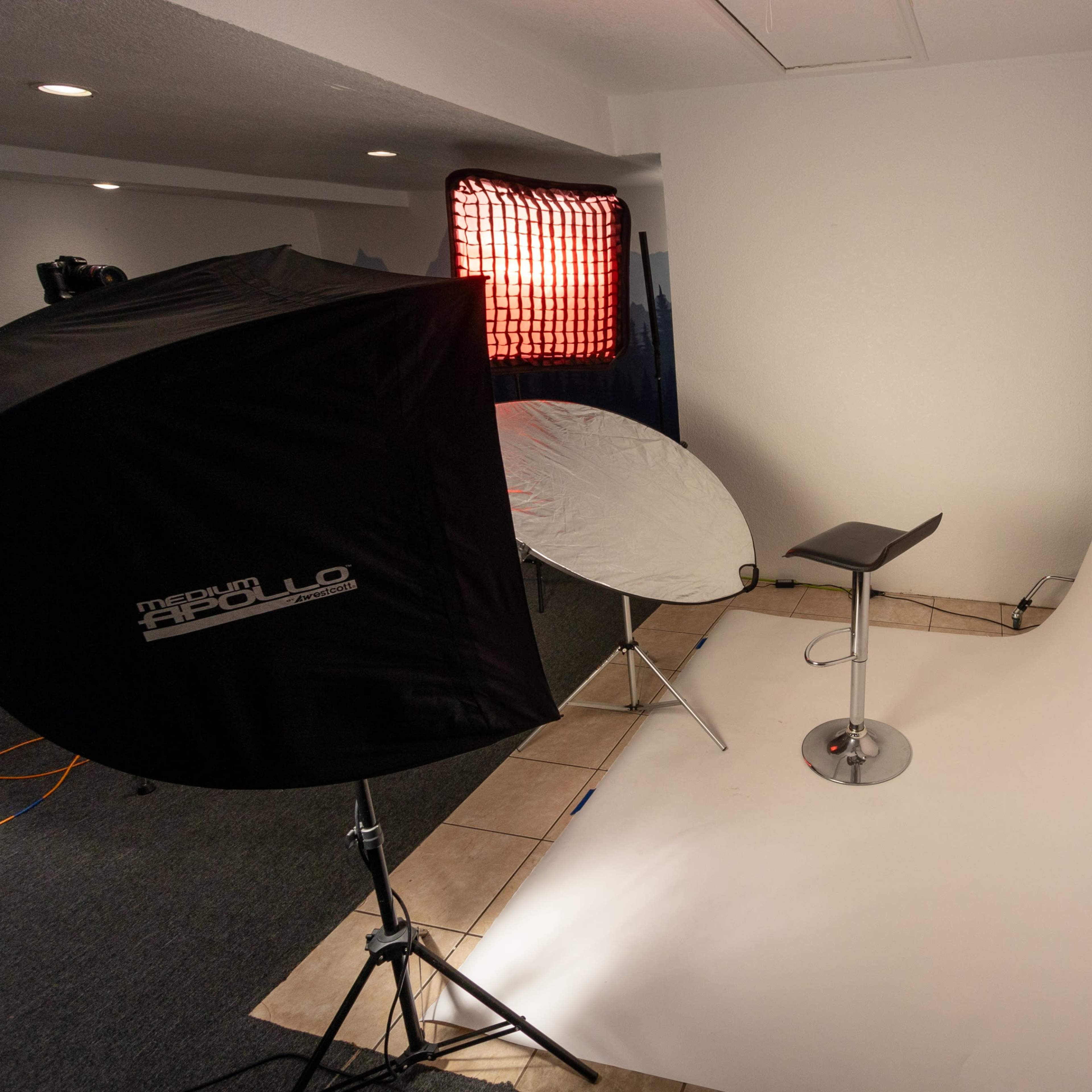 A photography studio setup featuring a curved backdrop, a high stool, and lighting equipment positioned to the side.