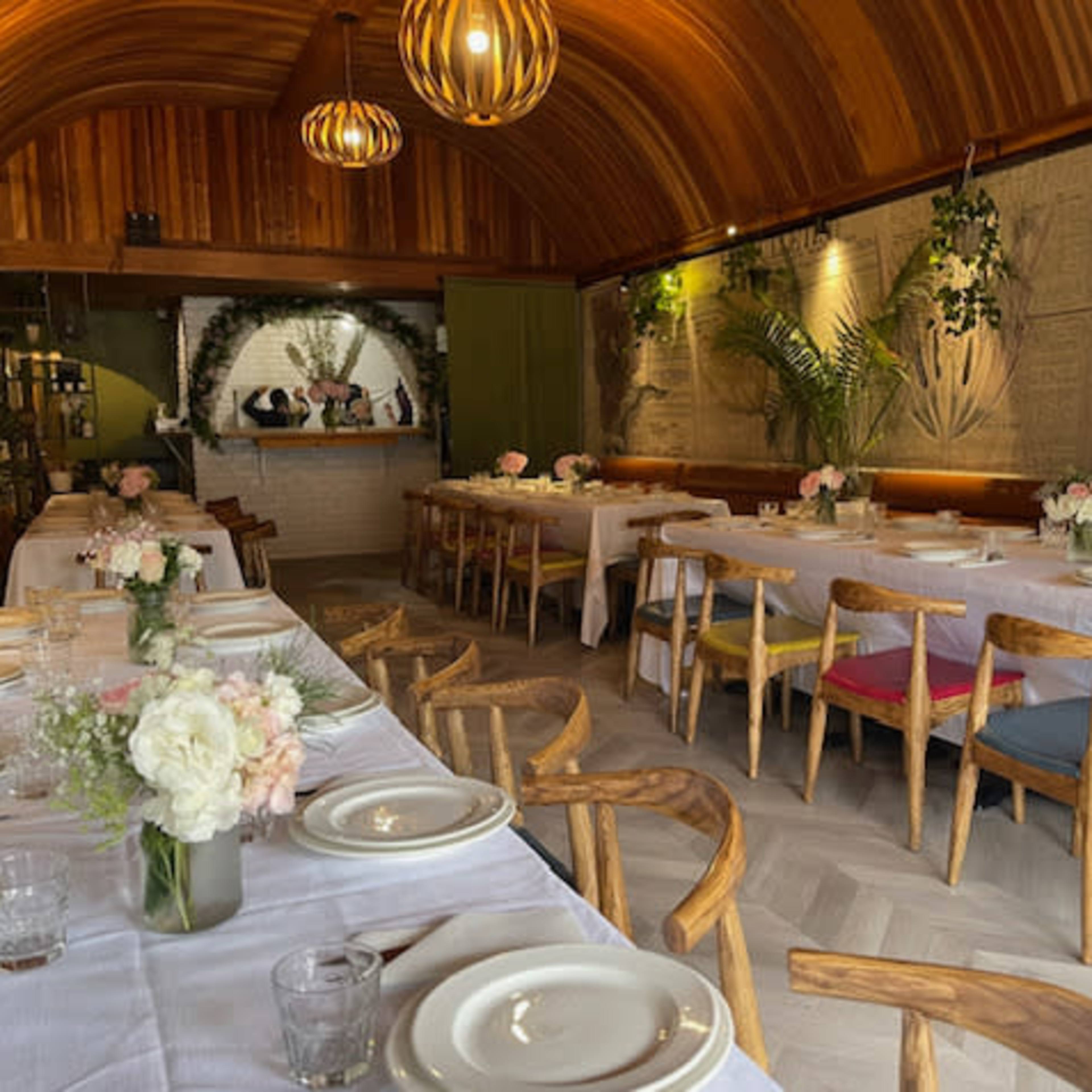 A restaurant interior with wooden paneling, long tables set for dining, and floral centerpieces.