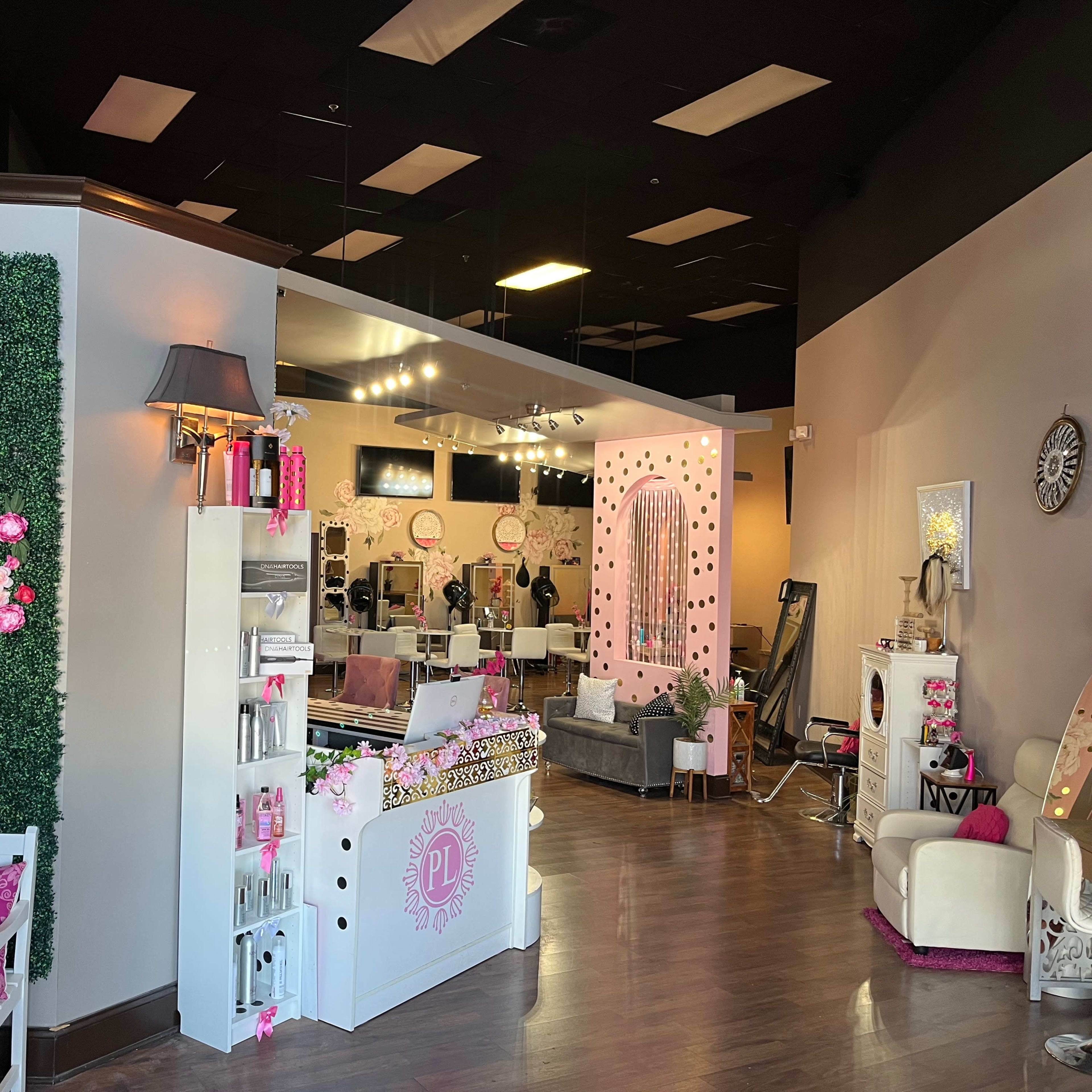 A beauty salon interior with a decorated green wall, stylish seating areas, and a reception desk adorned with pink accents.