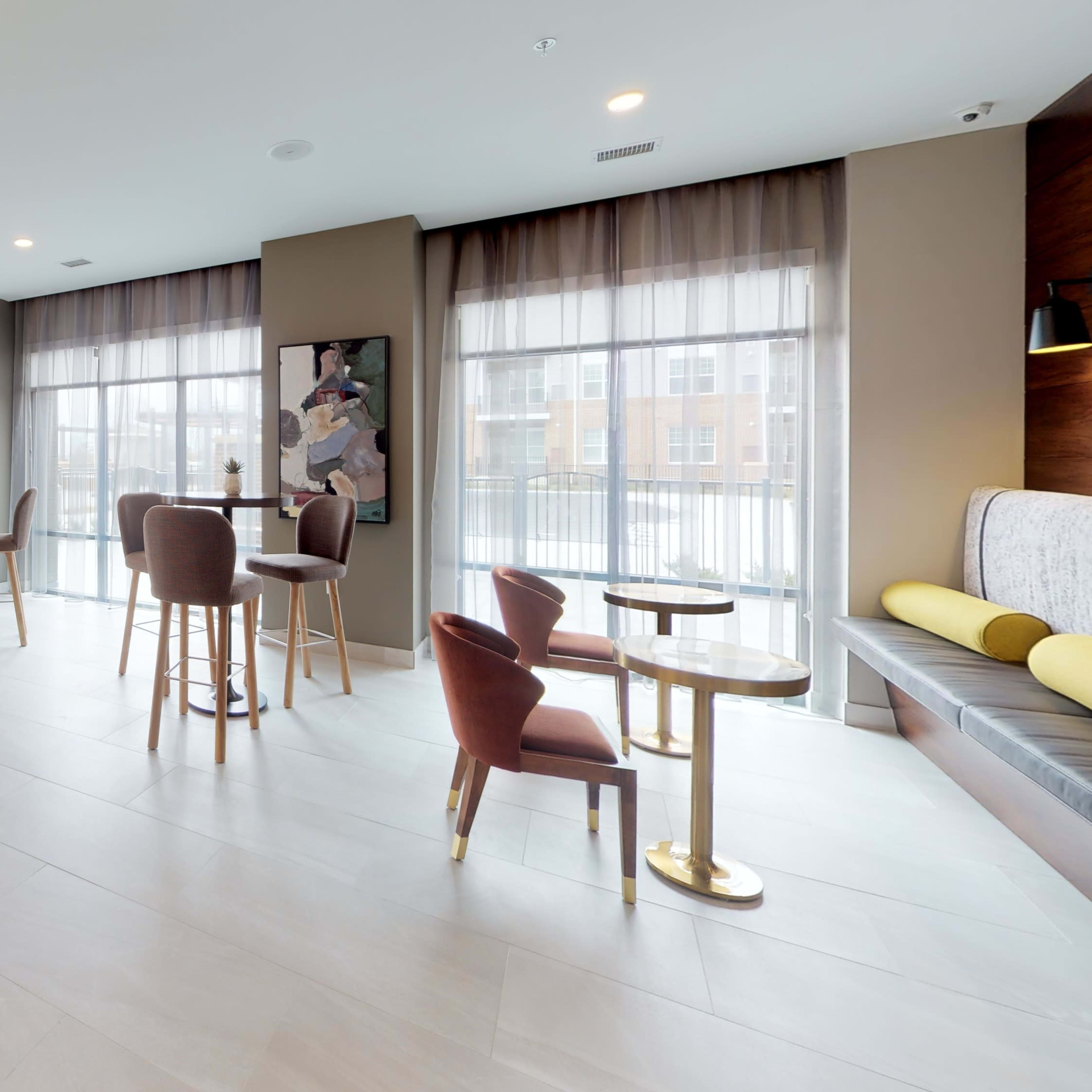 A modern gathering area with tables, chairs, and large windows allowing natural light to fill the space.
