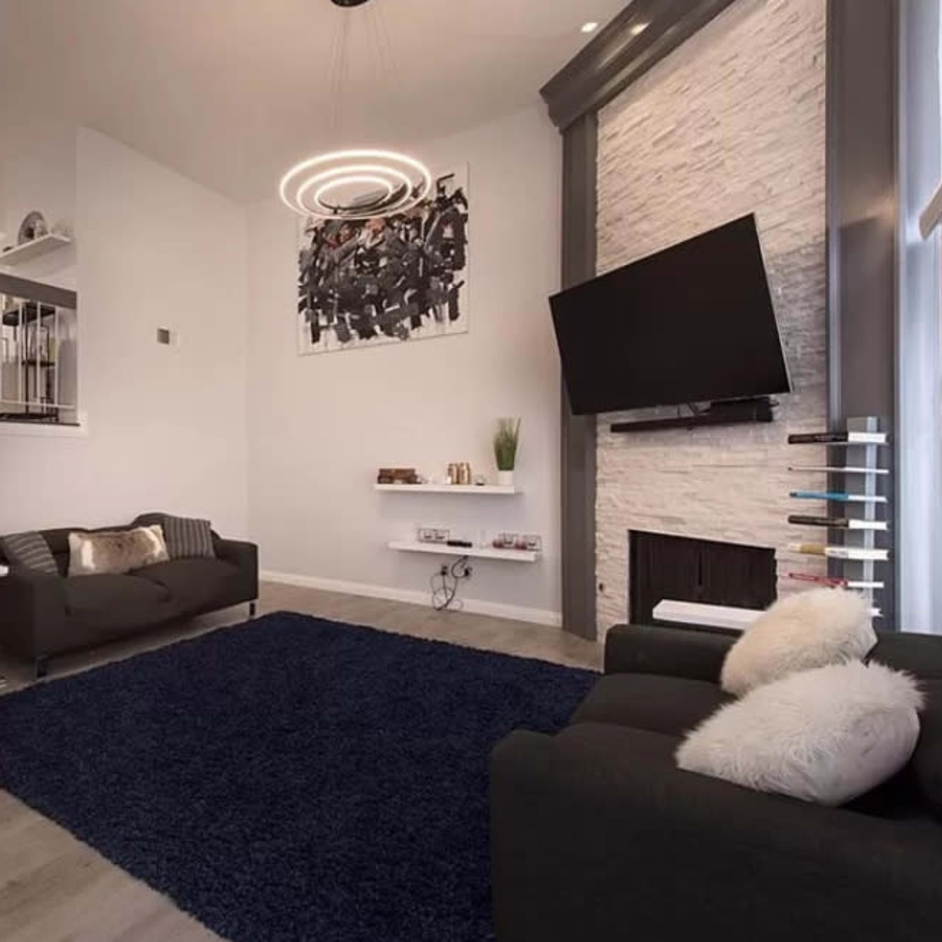 A modern living room with a staircase, a large rug, two sofas, and a wall-mounted television.
