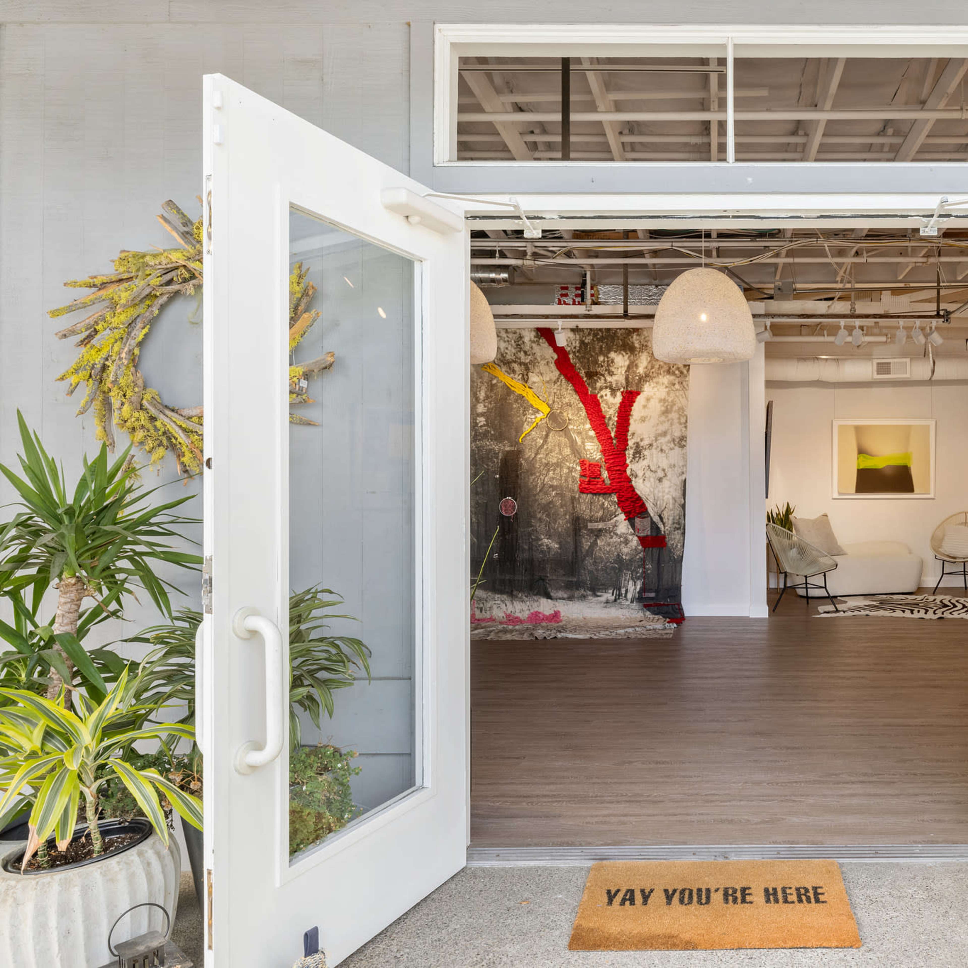 A welcoming entrance with double doors open, leading into a modern interior featuring artwork and plants.